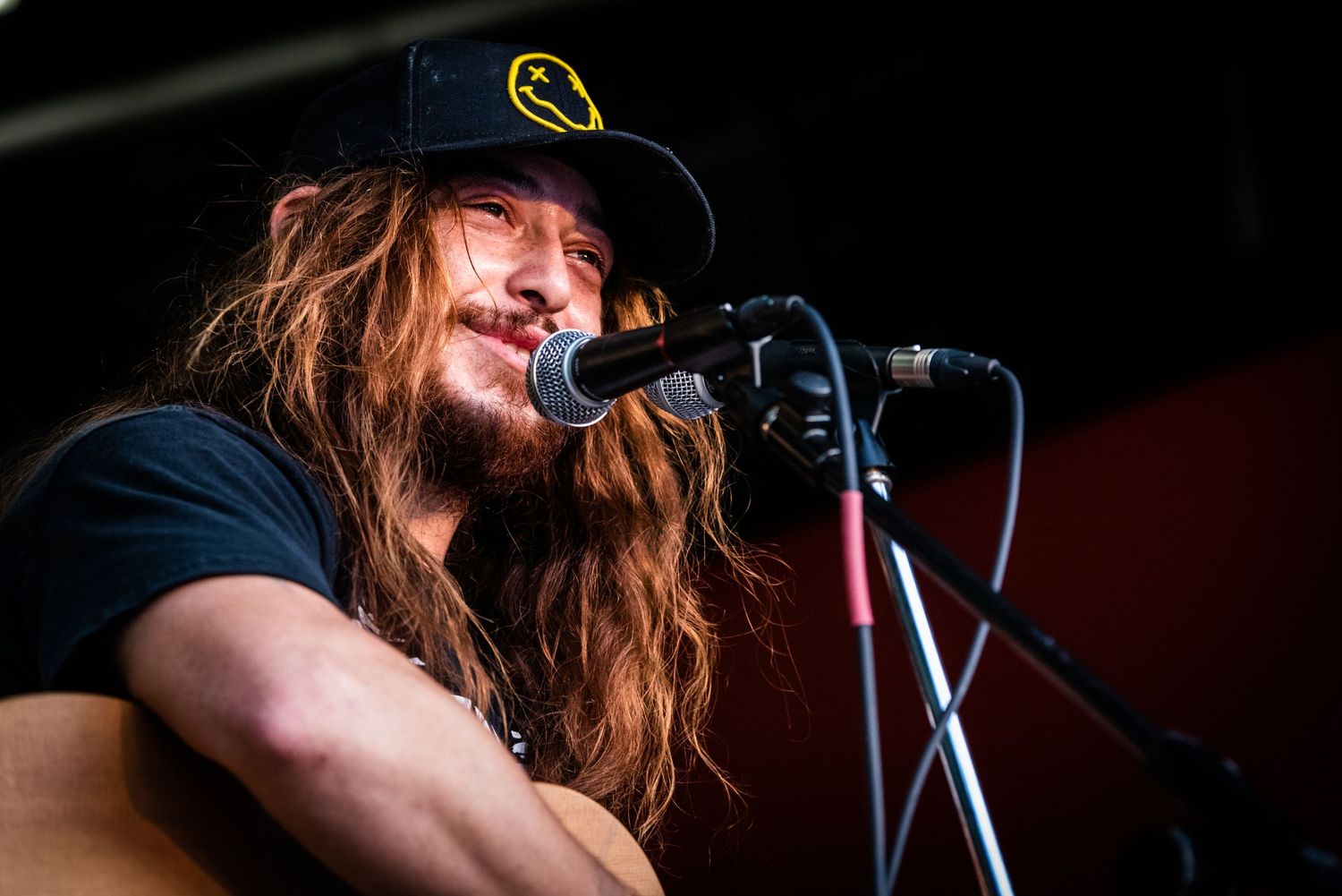 Musician with long hair and cap sings passionately into microphone during live performance.