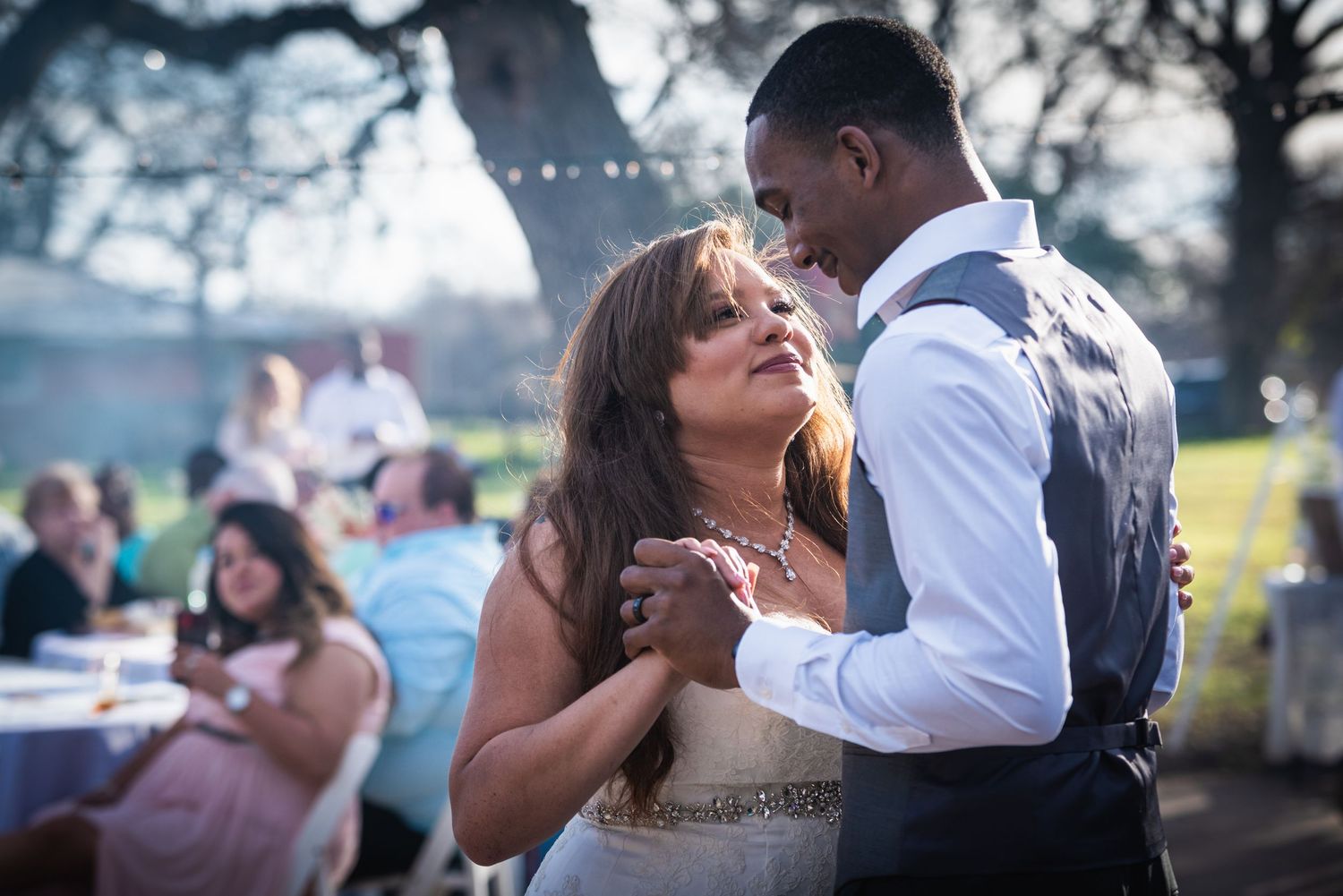 Couple shares intimate dance moment at outdoor wedding reception with guests in background.