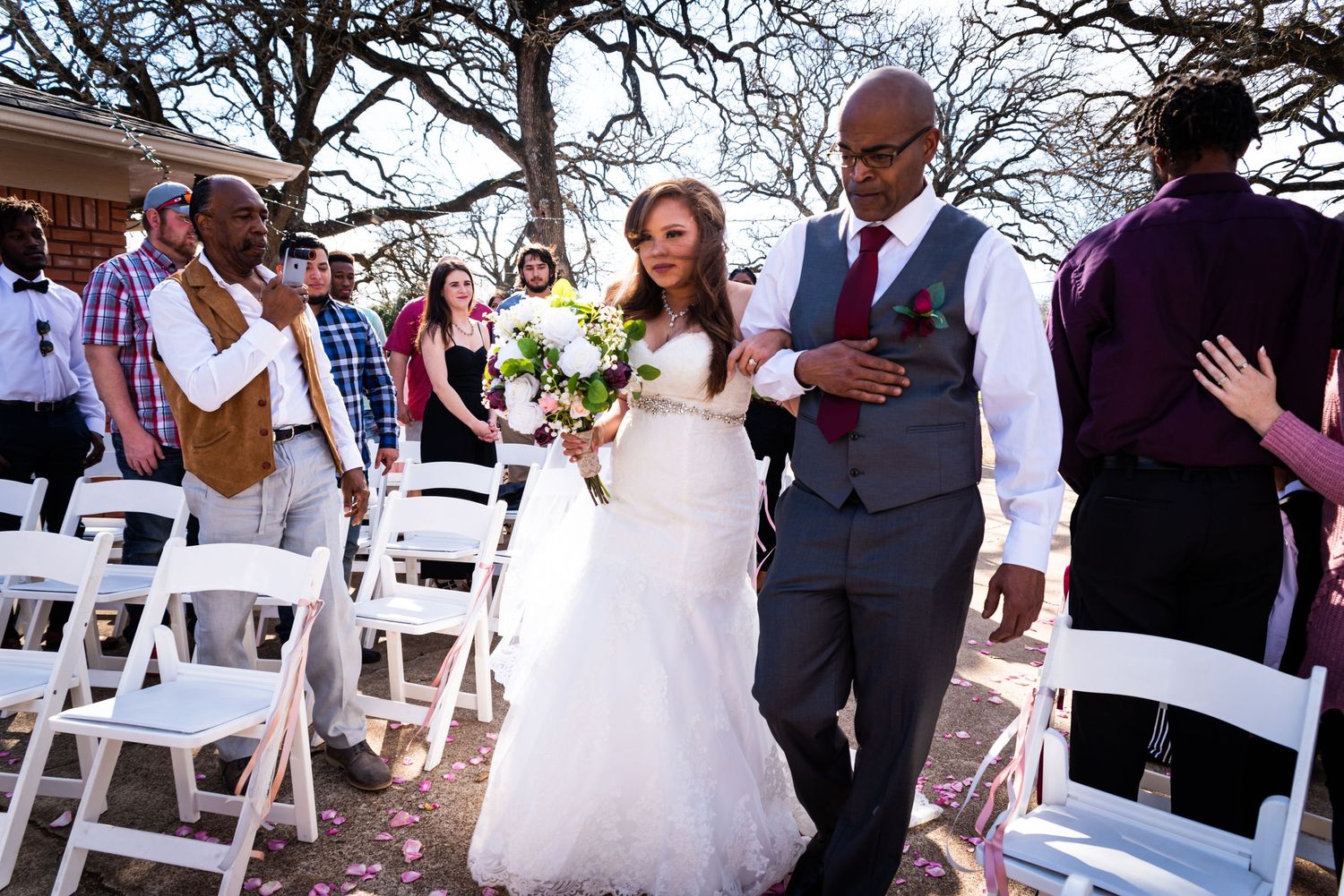 Newlyweds walk down the aisle together during an outdoor ceremony with white chairs.