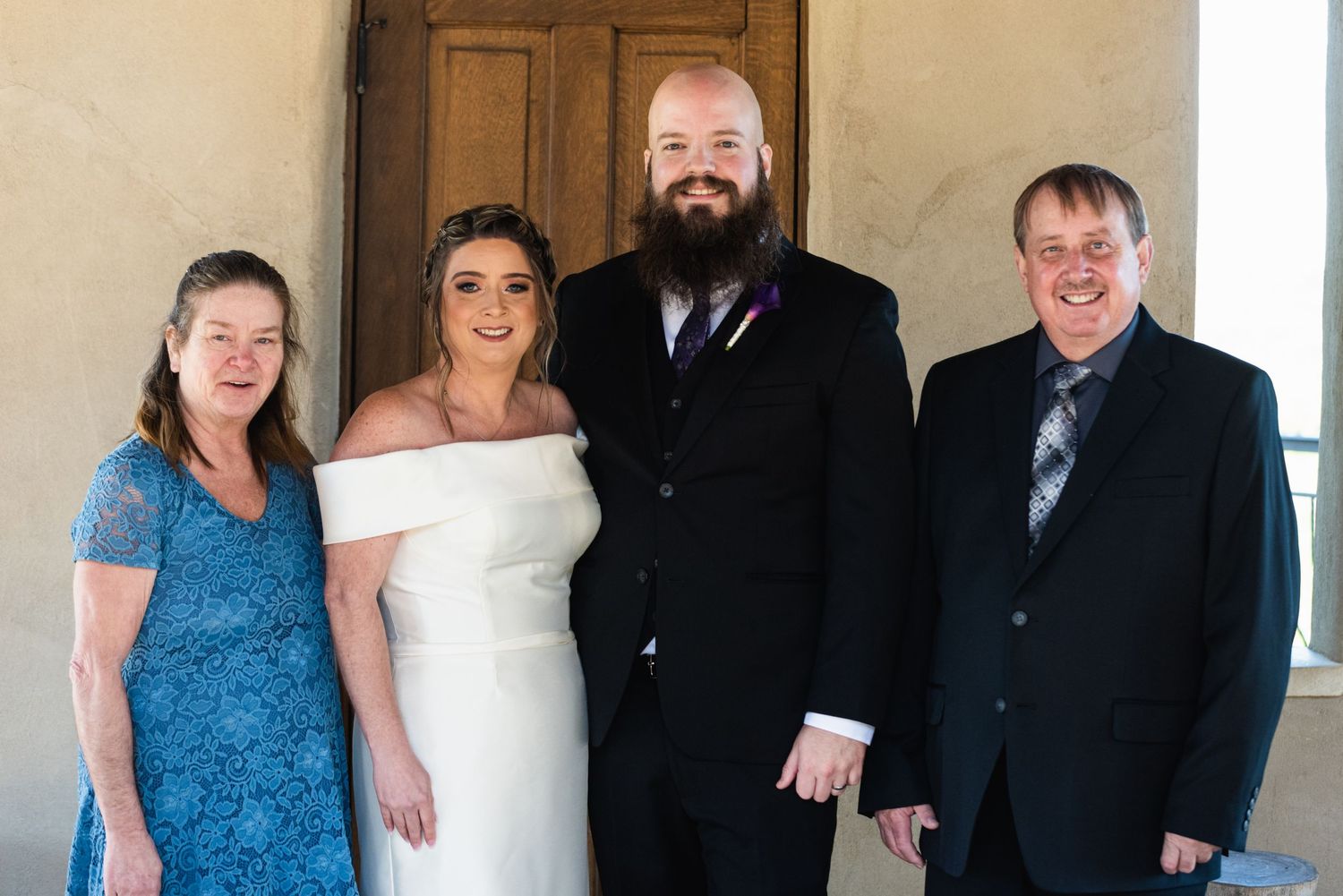 Small wedding party poses in formal attire outside a building.