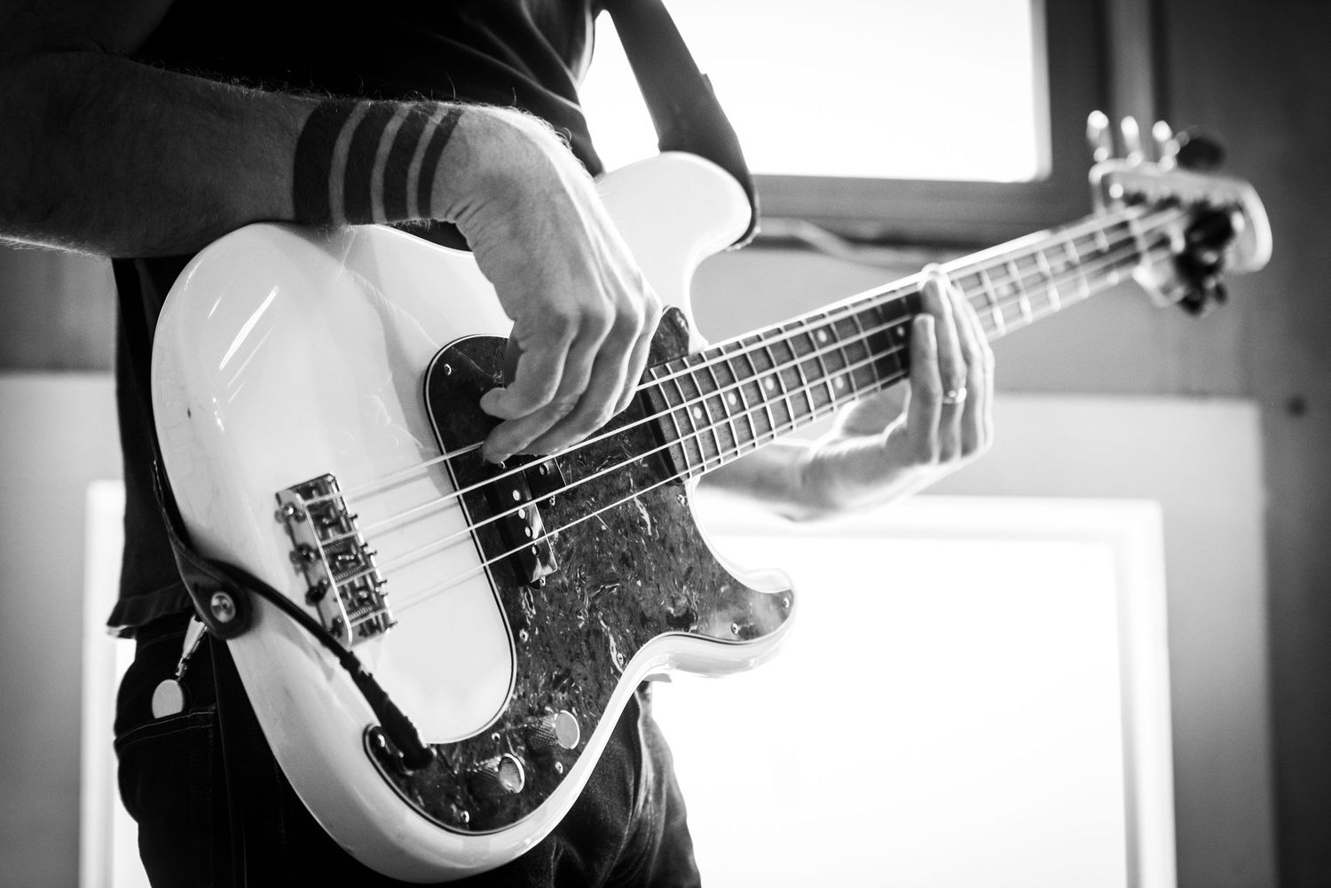 Close-up shot of hands playing a white electric bass guitar.