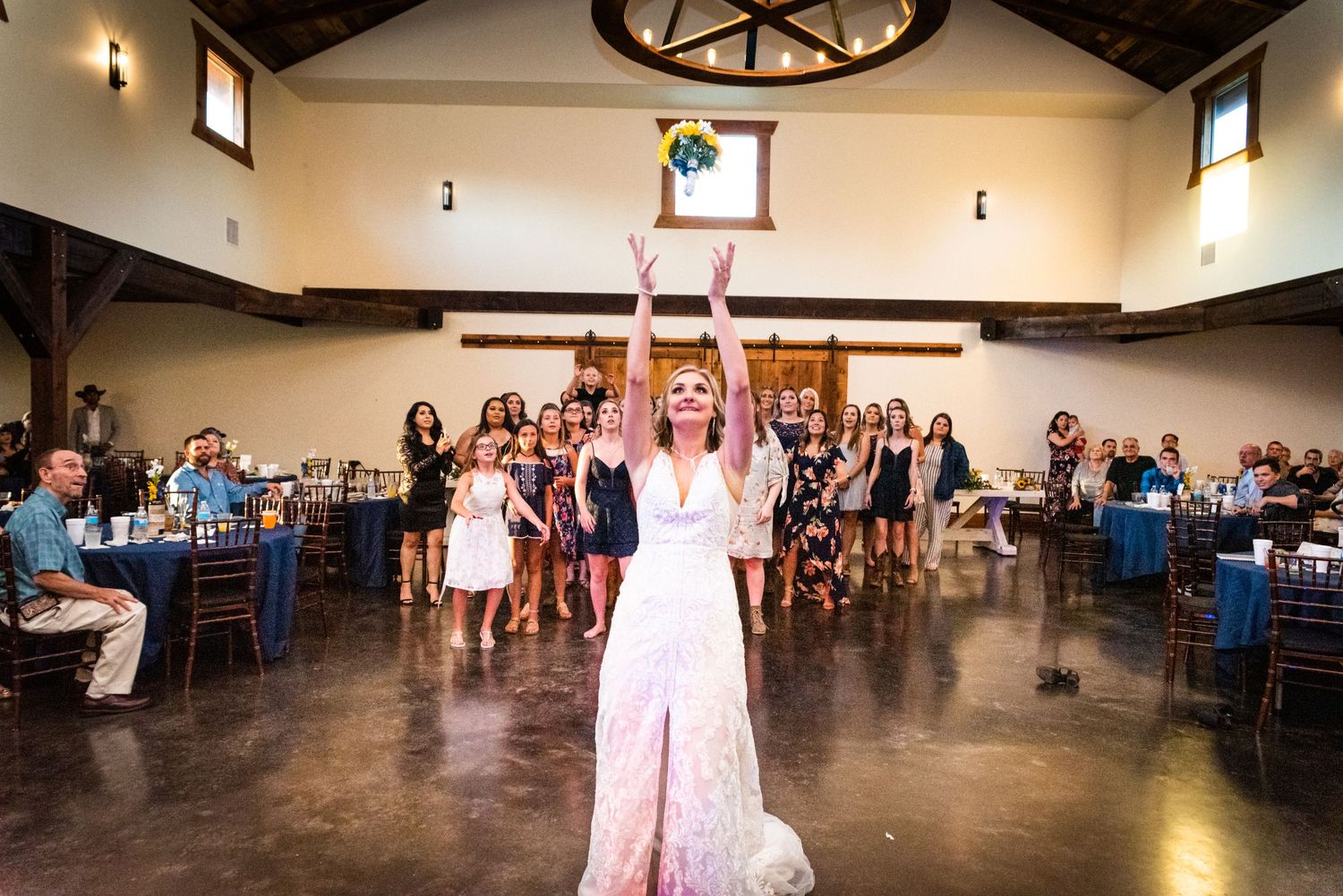 A bride tosses her bouquet during the traditional ceremony at an indoor wedding reception.
