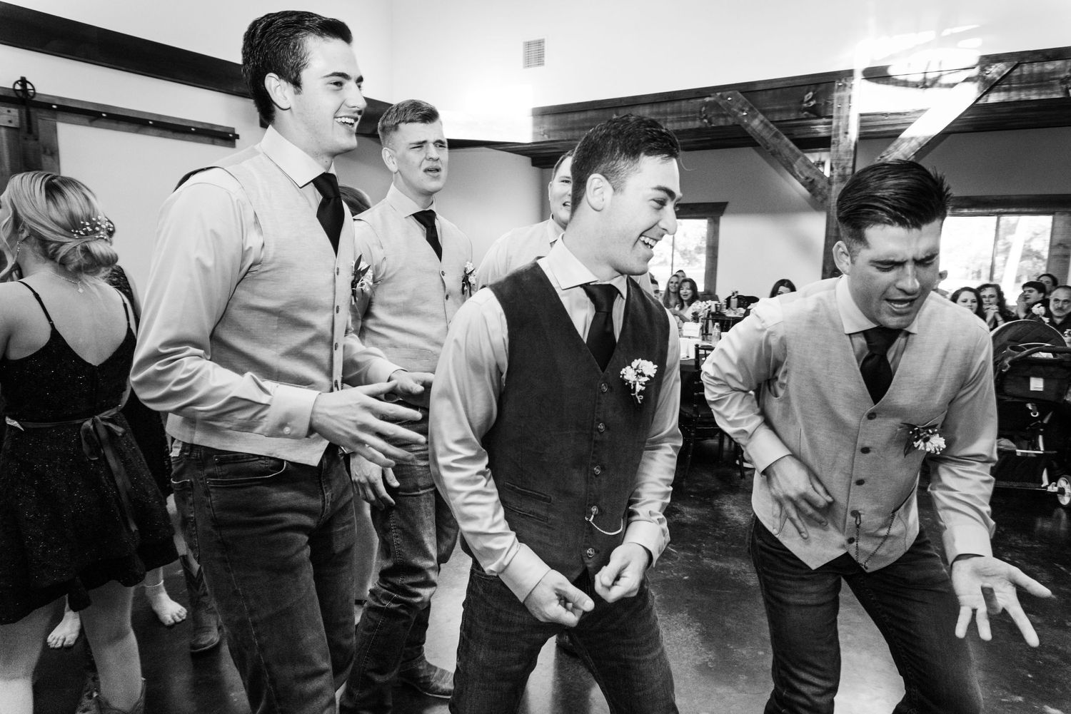 A black and white photo shows groomsmen having fun and dancing at the reception.