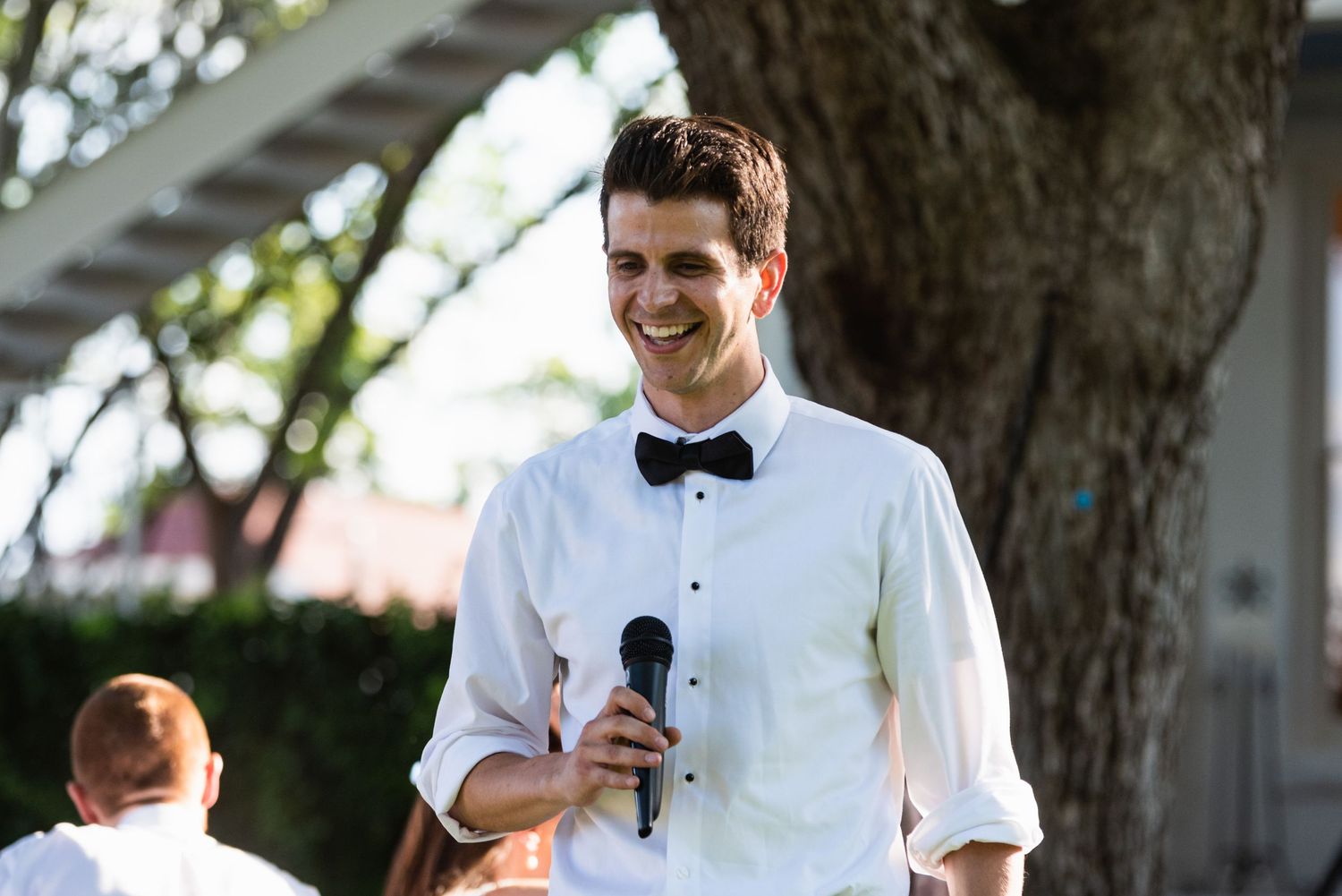Wedding speaker in white shirt and bow tie giving a speech outdoors.