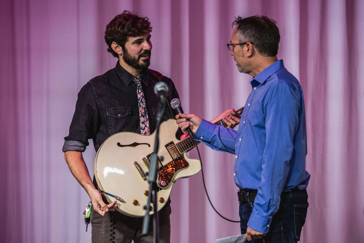 Interview taking place on stage with musician holding cream guitar.
