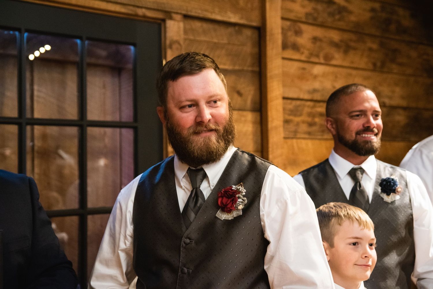 Groomsmen in vests and formal attire stand at attention during a wedding ceremony.