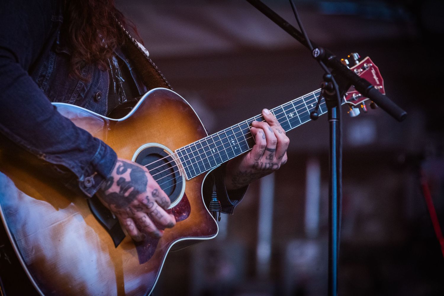 Close-up shot of tattooed hands playing an acoustic guitar during a live performance.