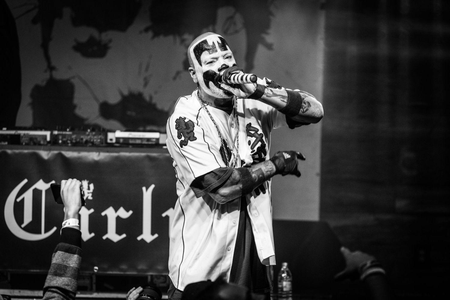 Concert performer in baseball-style jersey with face paint grips microphone during show.