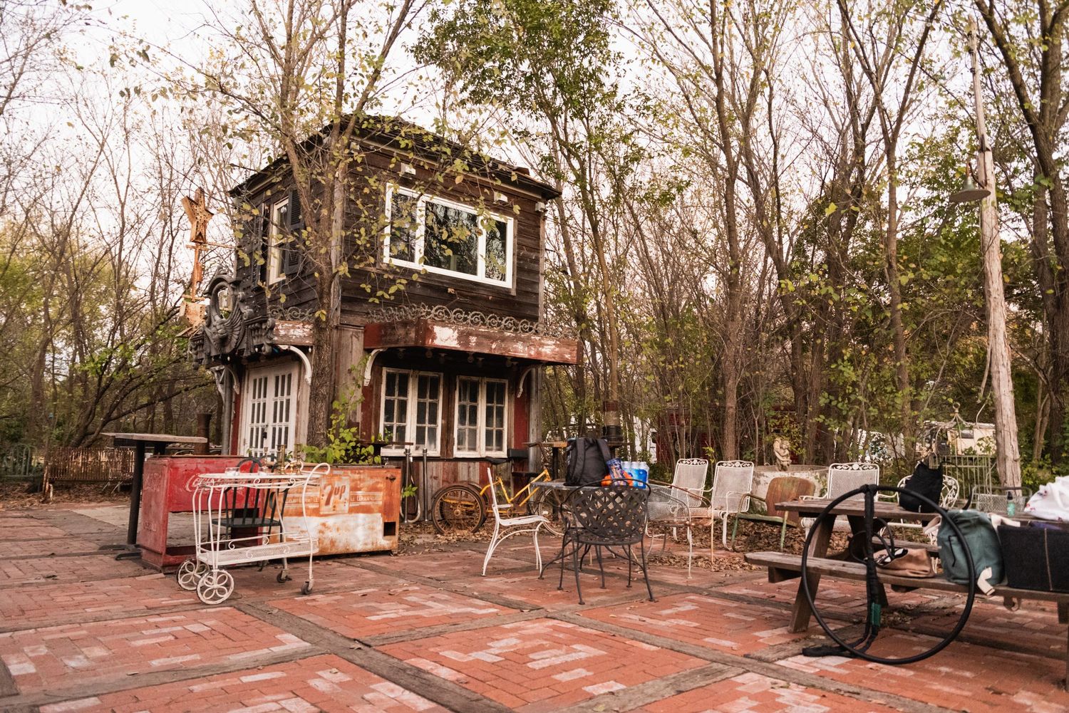 An outdoor rustic two-story wooden building with red brick patio and scattered chairs.