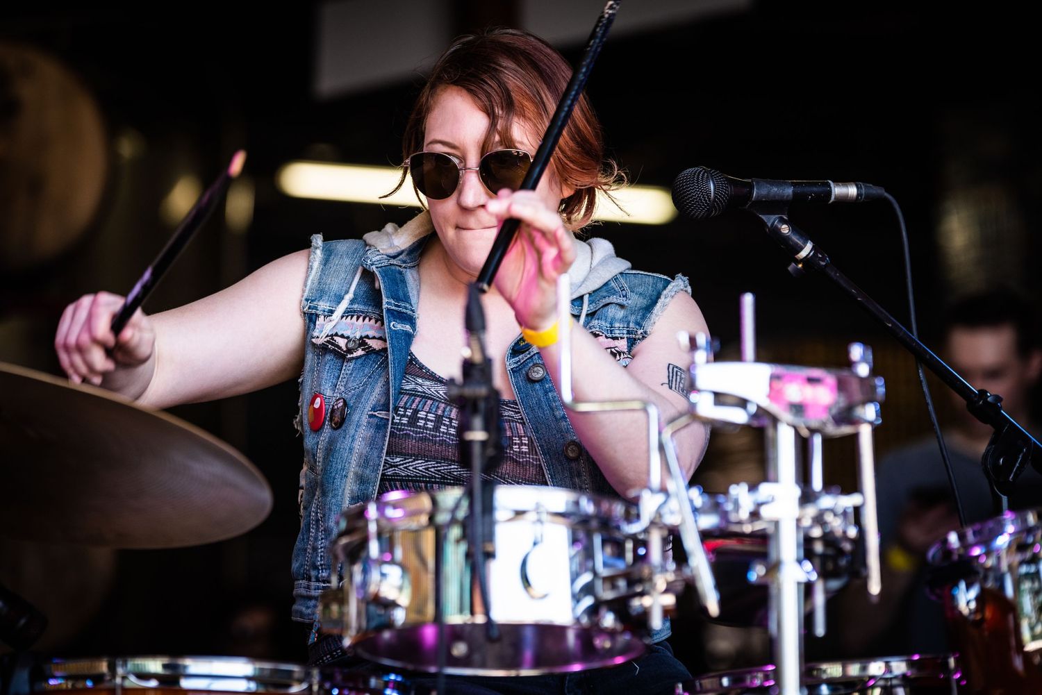 Drummer in denim vest plays with passion during live music performance.