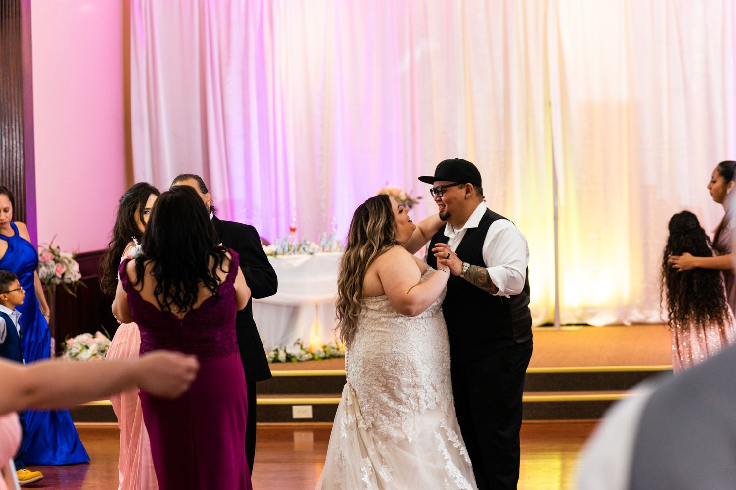 Couple shares romantic first dance at their wedding reception with pink and white backdrop.