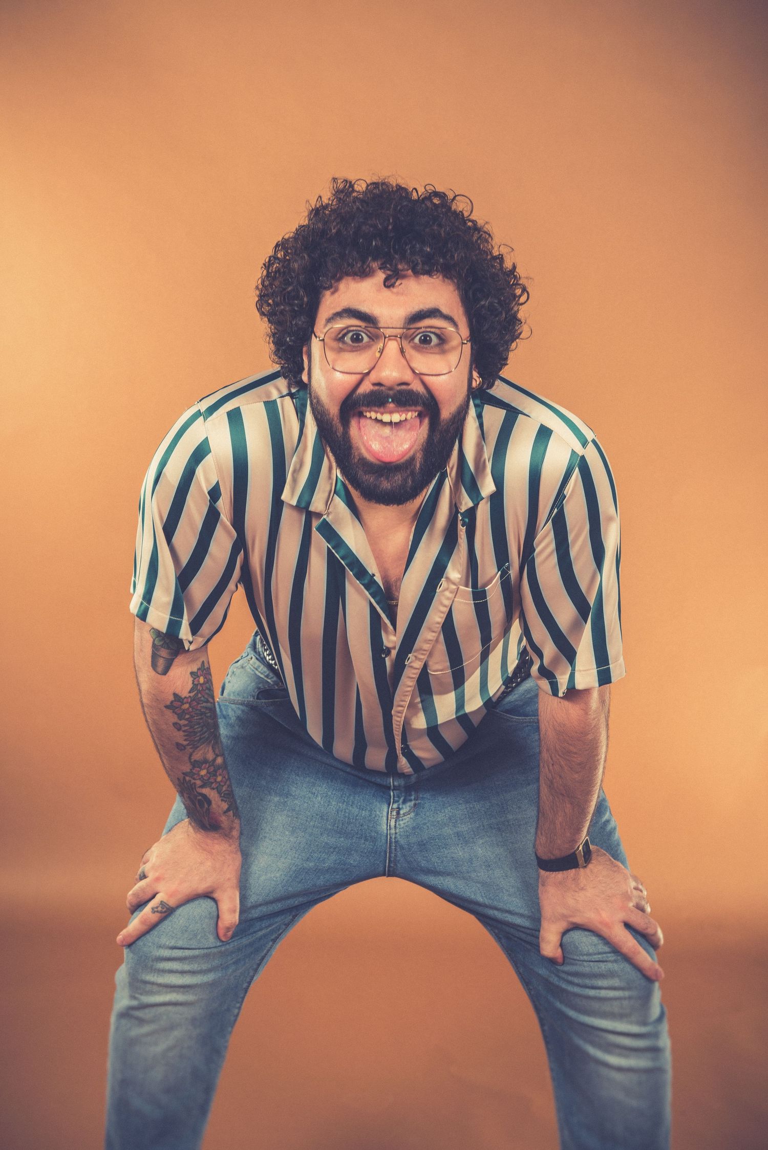A person in a striped shirt and jeans poses energetically against an orange backdrop.