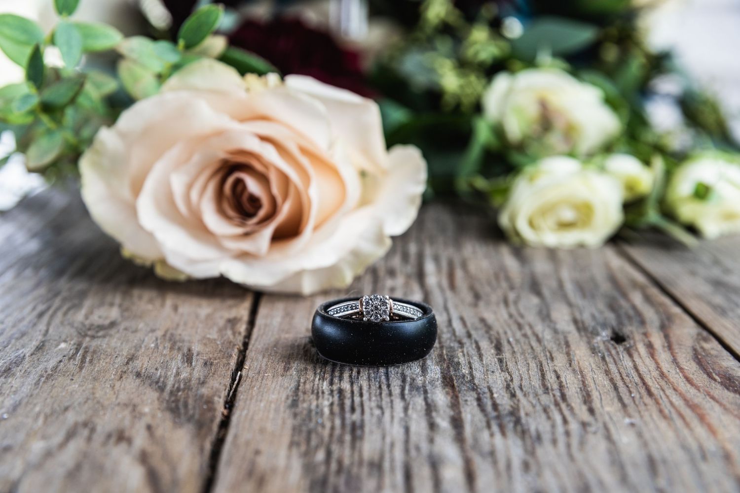 Wedding rings displayed next to delicate pink roses on weathered wooden surface.