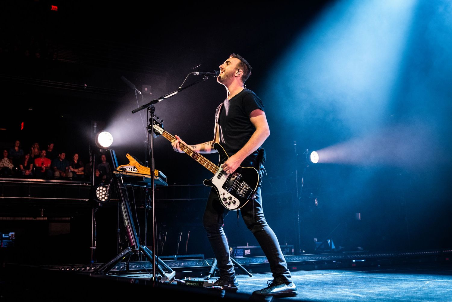 Musician performs energetically on stage with guitar under dramatic blue spotlight during live concert performance.