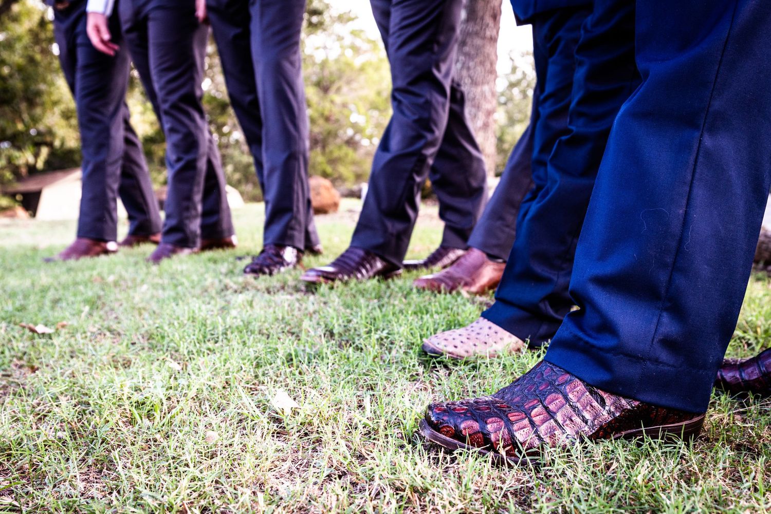 Row of dress shoes and pants on grassy ground showing wedding party footwear.