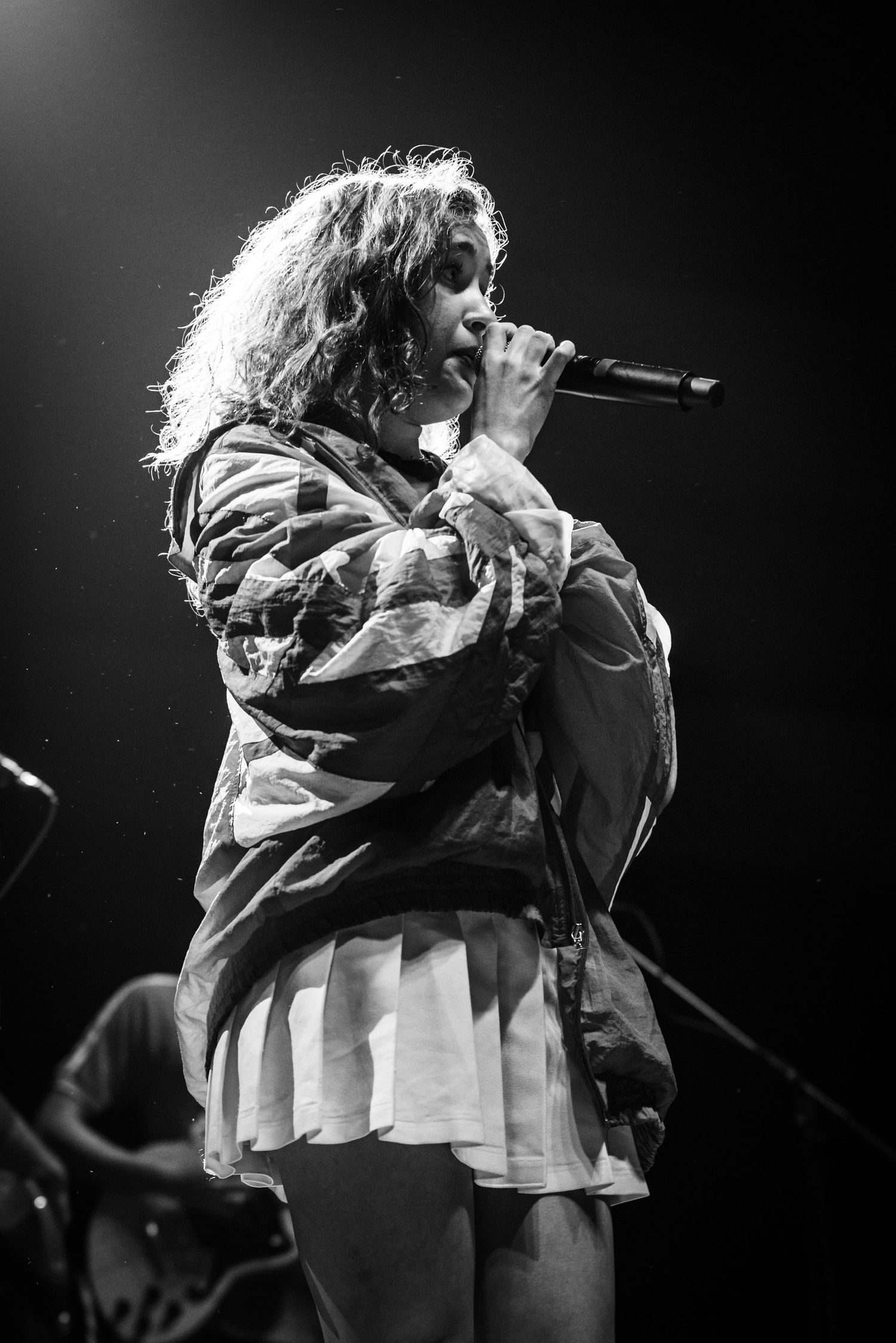 Black and white concert photo of a performer singing in an oversized jacket.