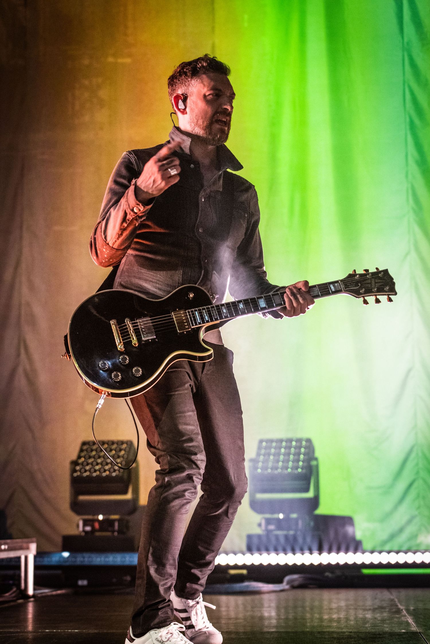 Rock musician playing electric guitar against colorful gradient background on stage.