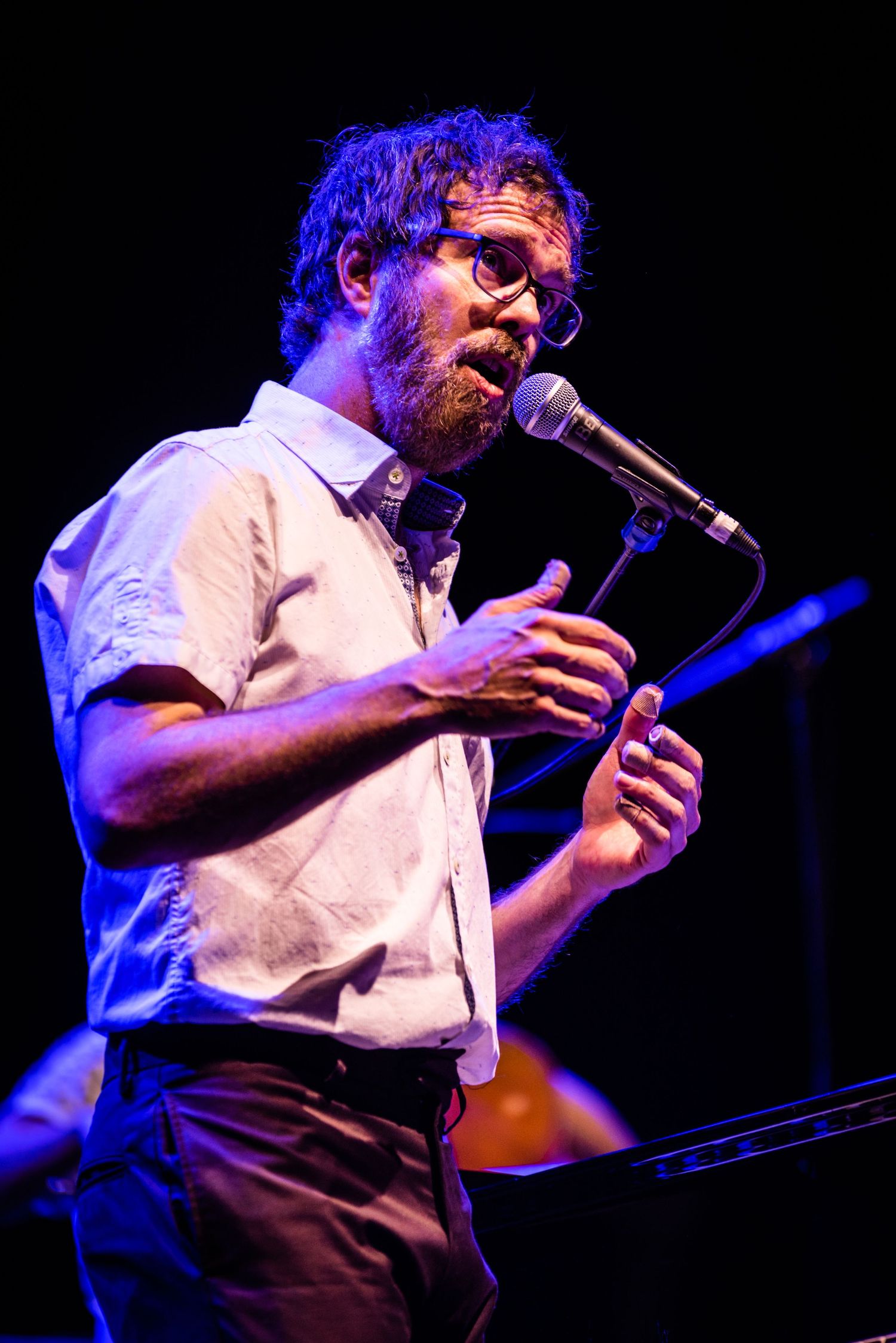 Performer in a white shirt singing passionately into microphone under blue stage lighting.