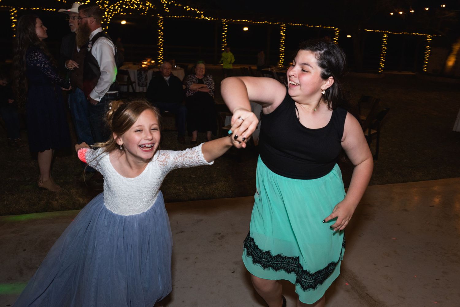 Two people dancing energetically at a wedding reception under string lights.