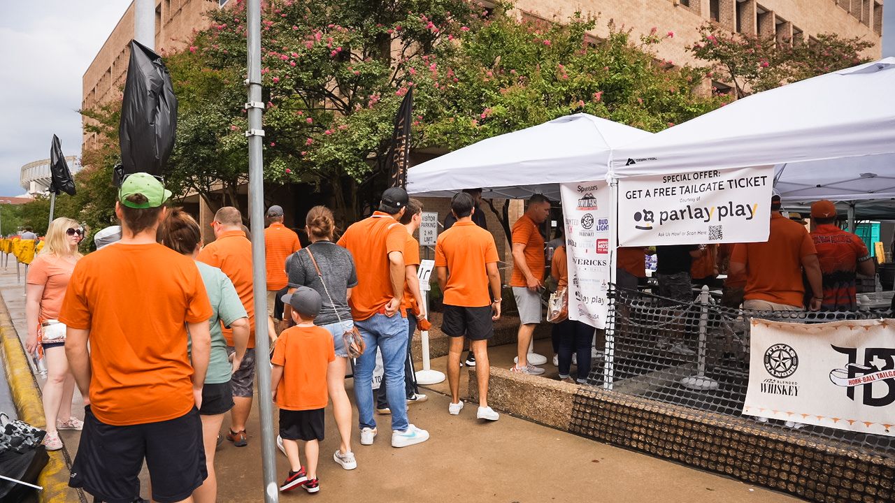 Crowd in orange shirts walking past vendor tents at outdoor festival.