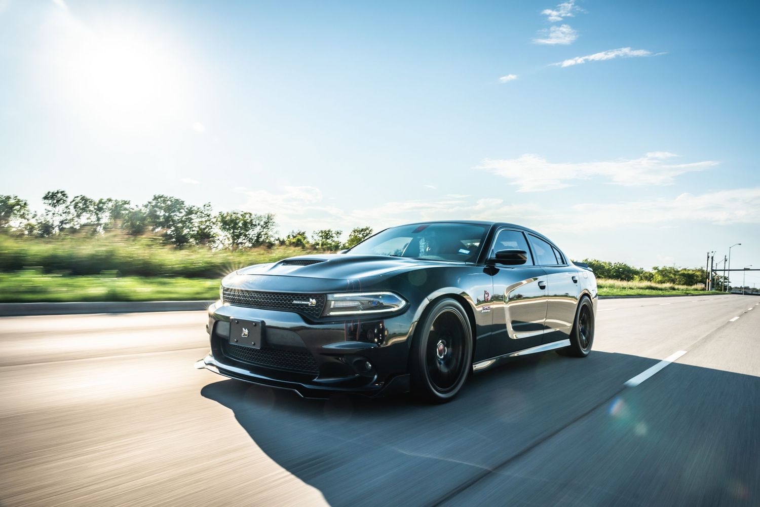 Black Dodge Charger SRT cruising on open road with blue sky background.