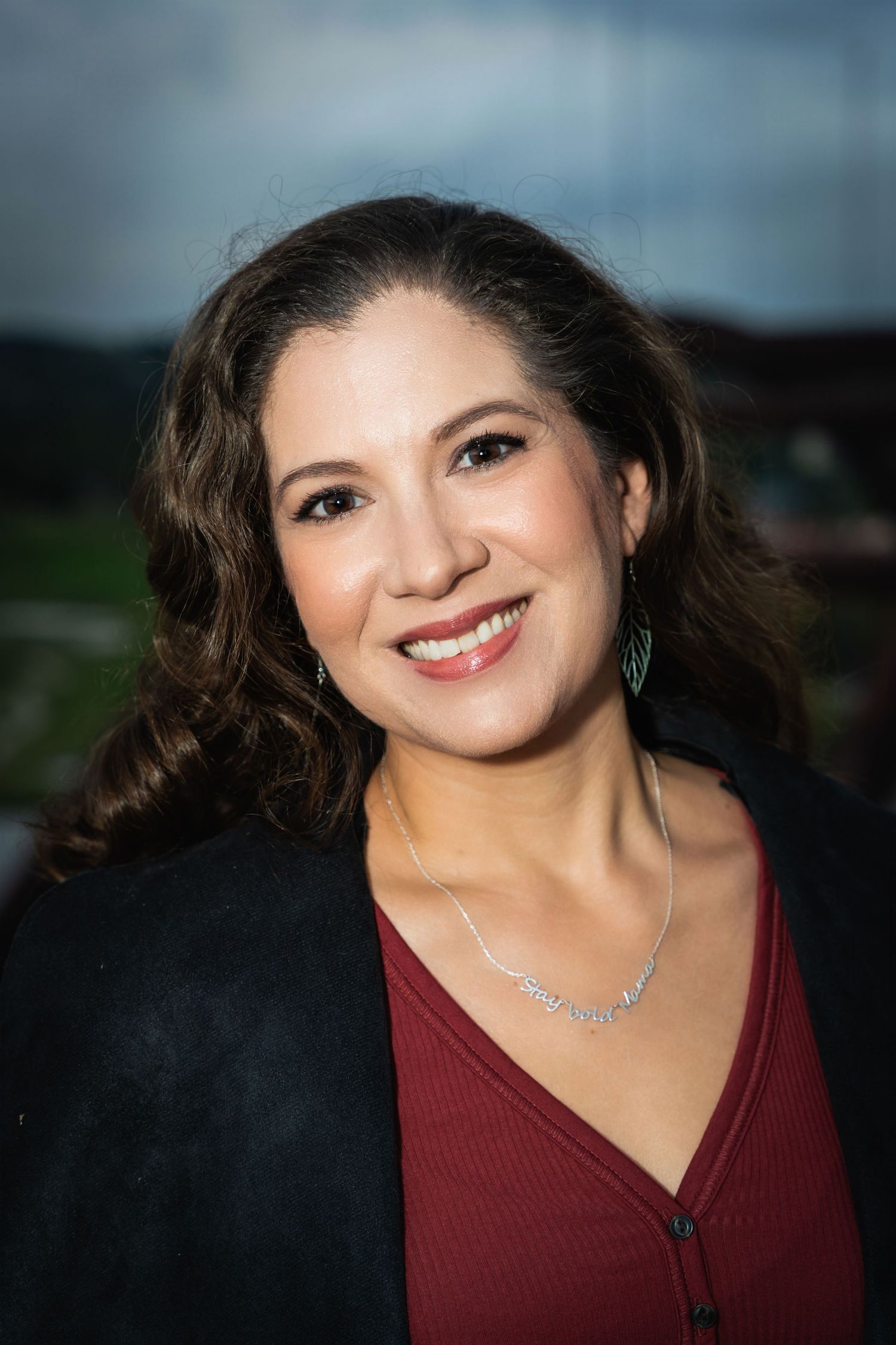 Professional headshot portrait of someone in a burgundy top and black cardigan smiling against a blurred background.