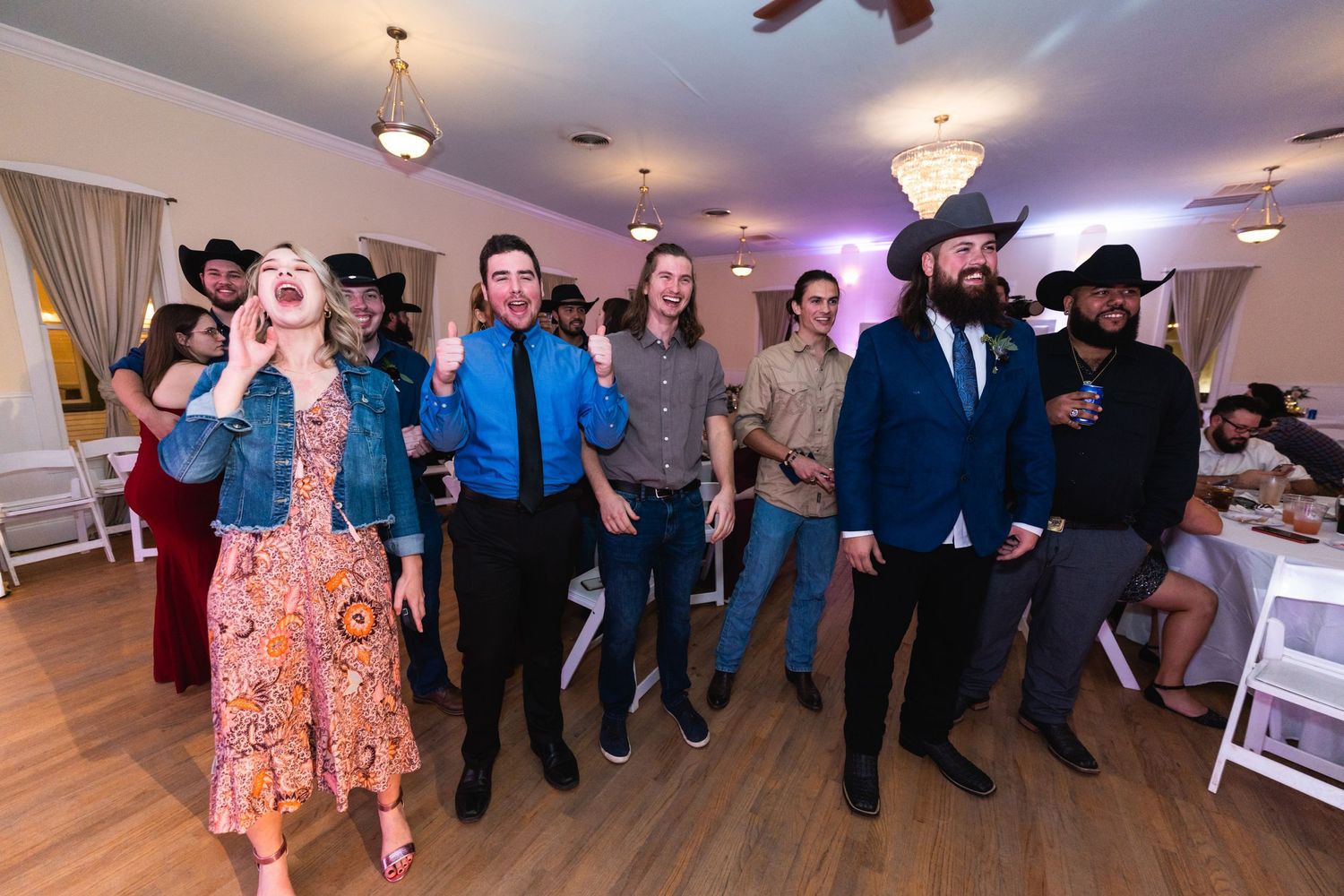 Wedding guests perform a choreographed line dance at a reception venue.
