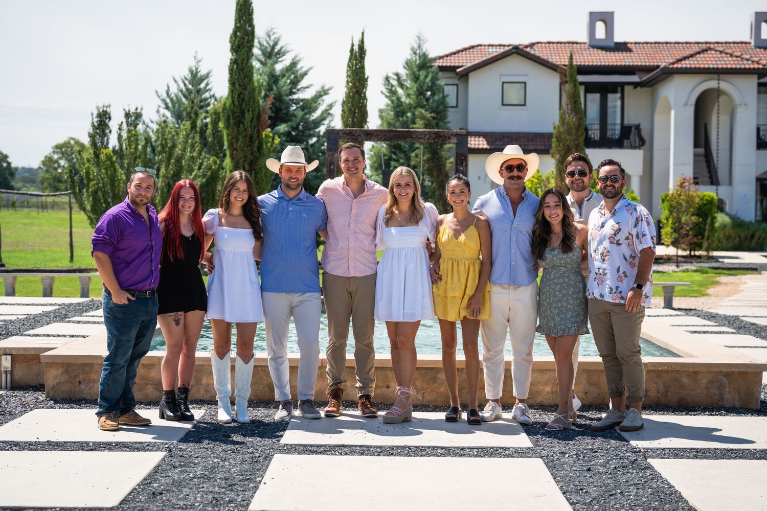 A group photo of family and friends gathered outdoors by a luxurious pool and villa.