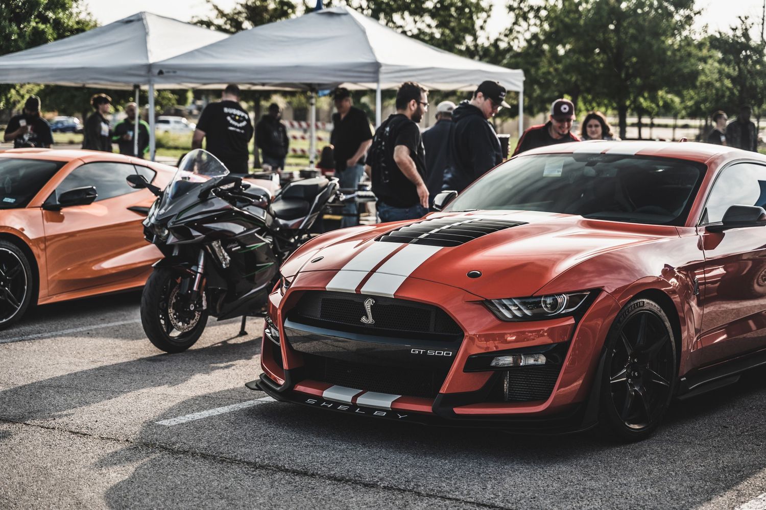Red Mustang GT500 and motorcycle on display at an outdoor car meet.
