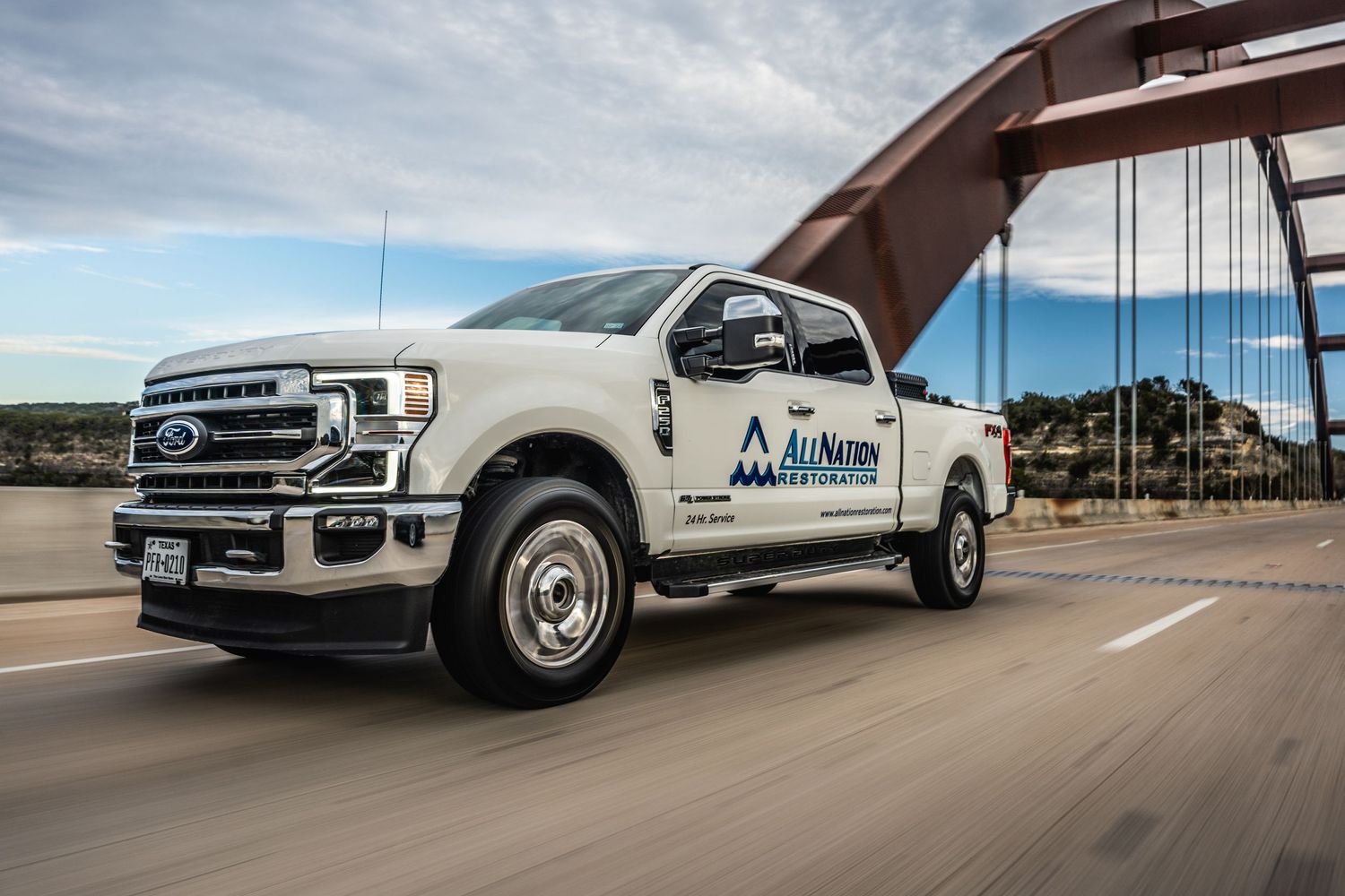White Ford truck with company branding drives across a bridge under cloudy skies.