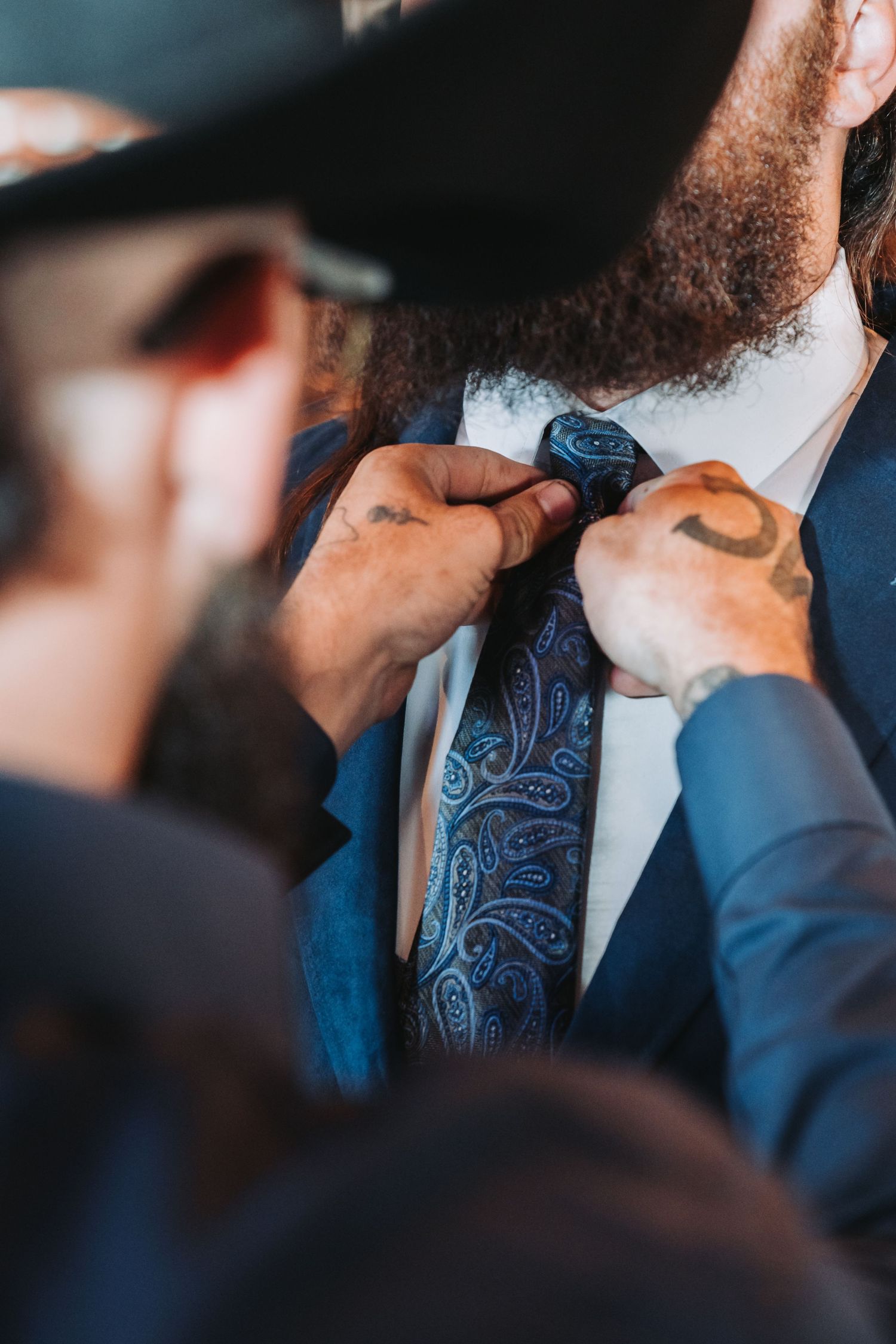 Close-up shot of hands adjusting a blue patterned tie on formal attire.