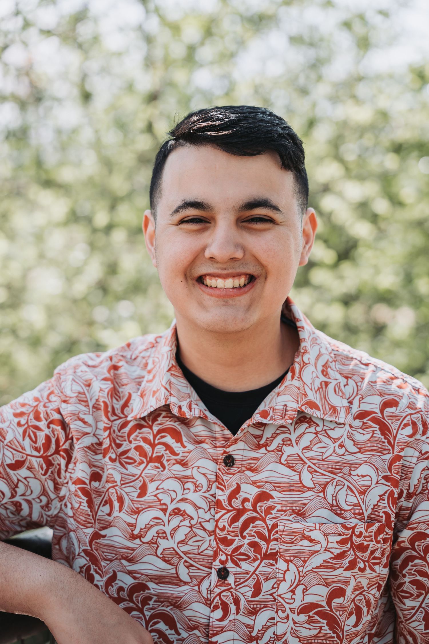 Outdoor portrait of someone wearing a patterned red and white Hawaiian shirt against blurred foliage.