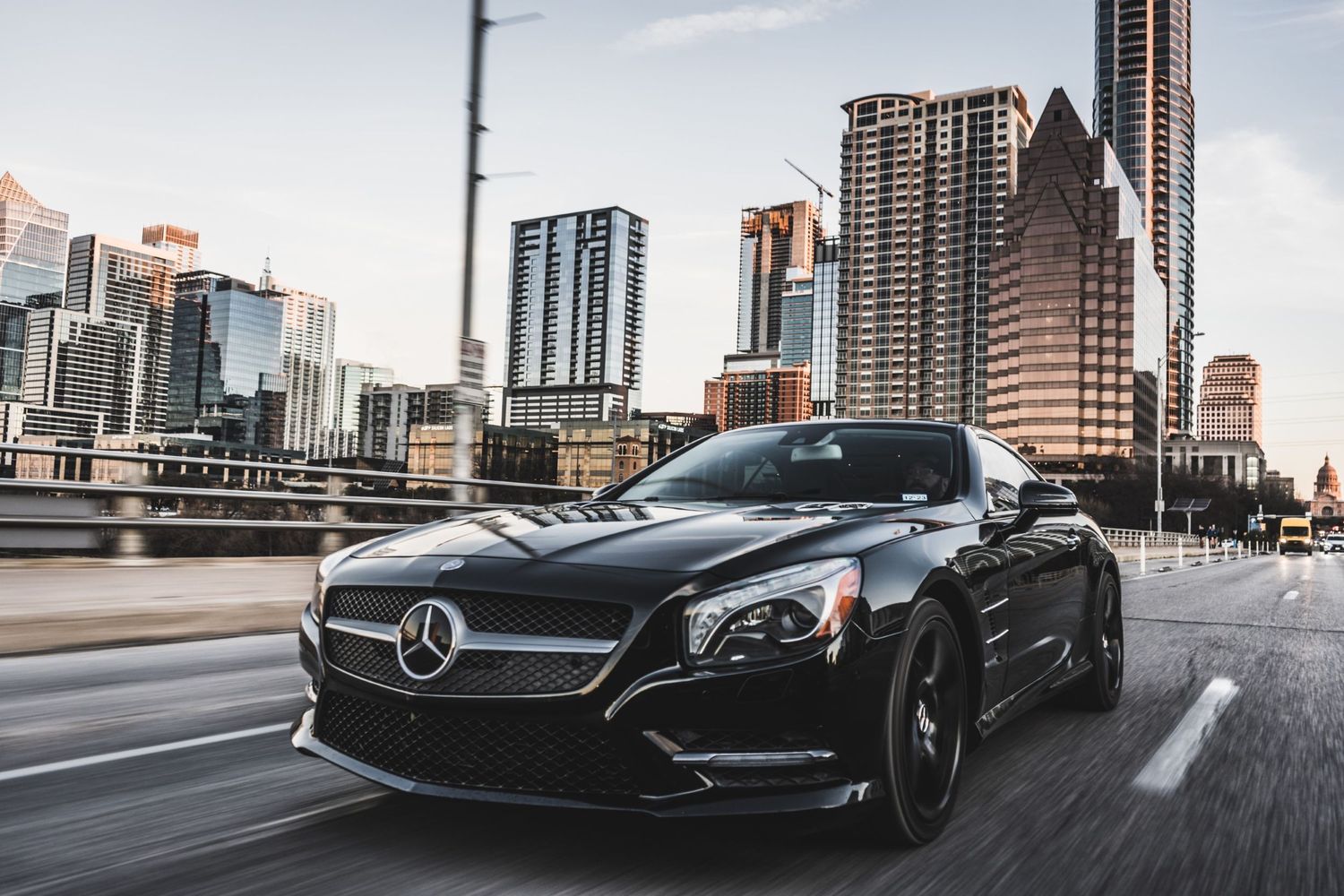 Sleek black Mercedes sports car speeding through downtown with modern buildings.