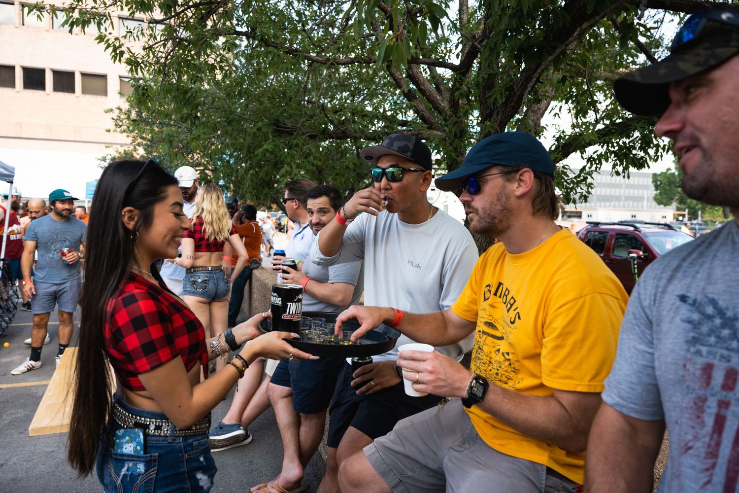 A lively tailgating scene with fans interacting outside under trees.