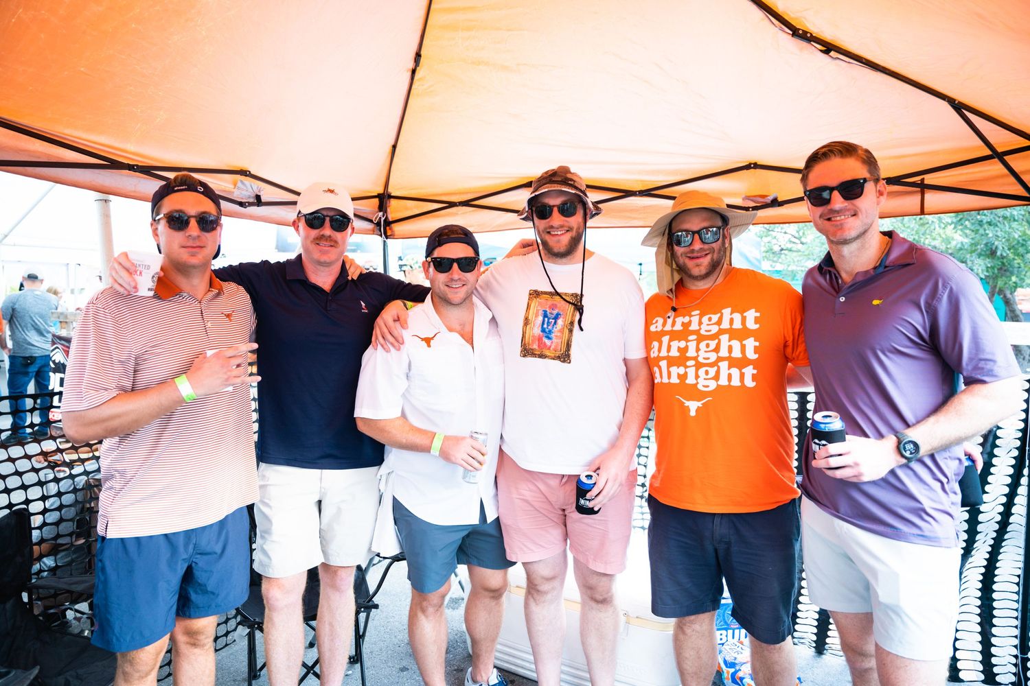 Group of friends posing together at an outdoor event under an orange tent.