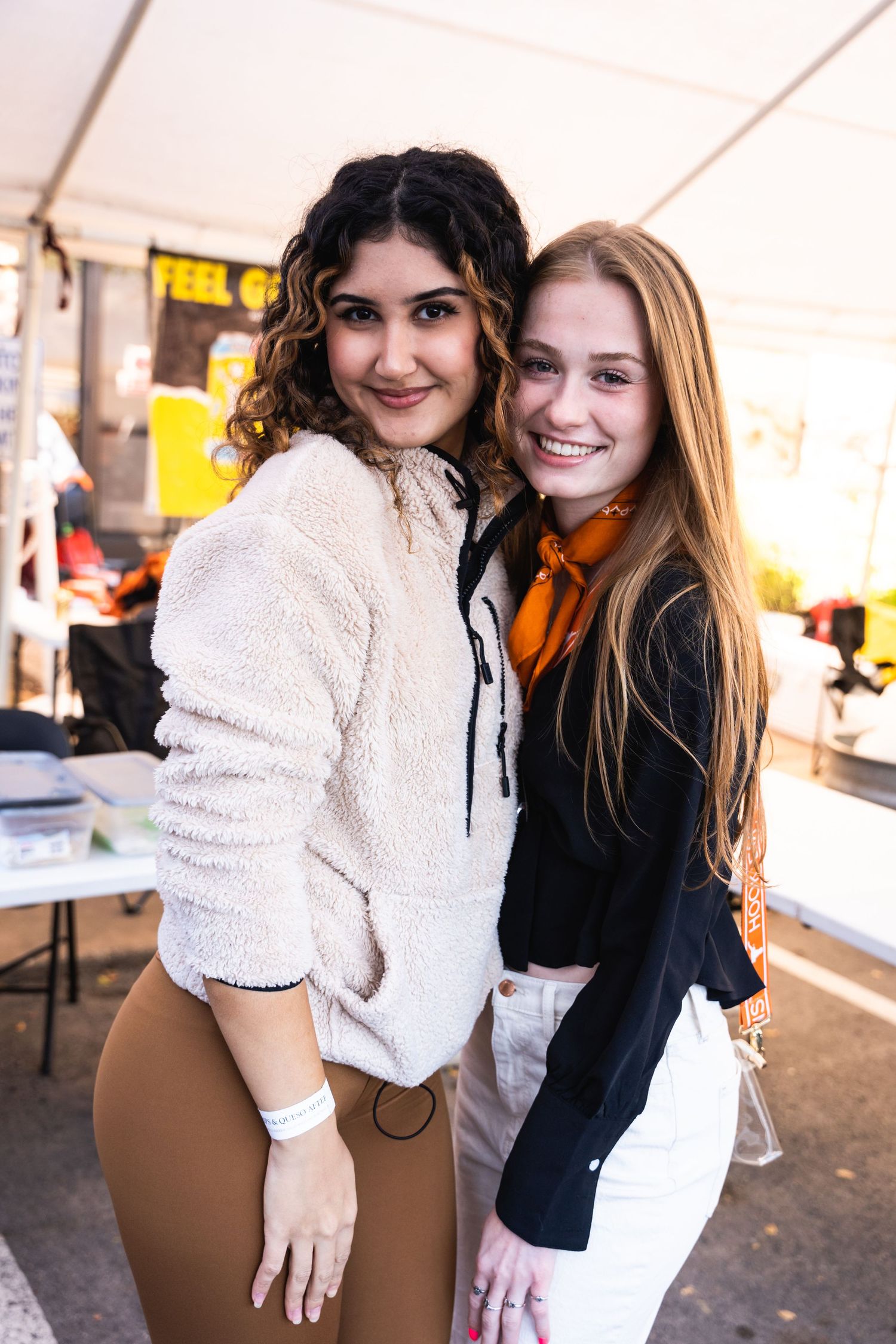 Two friends smiling together at an outdoor event wearing casual winter attire.