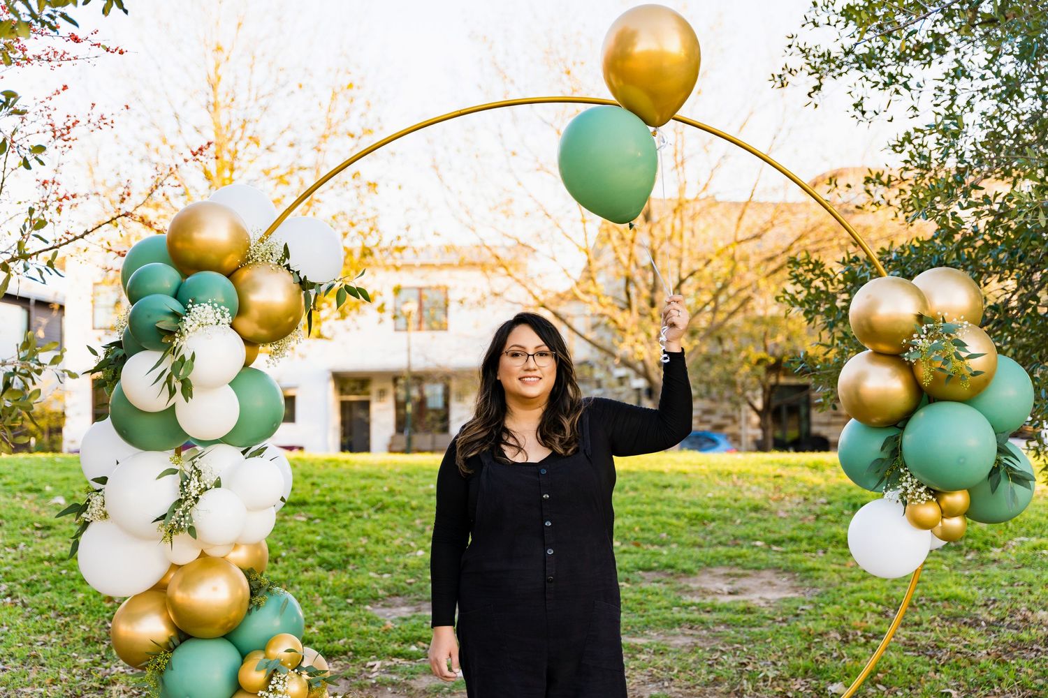 Person beneath a golden hoop arch decorated with mint and white balloons in autumn scenery.