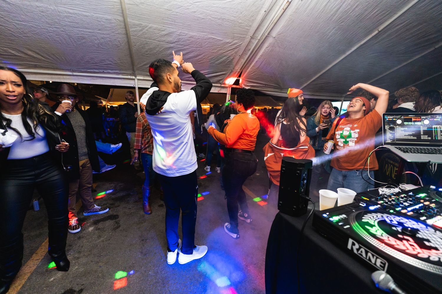 People dancing under a tent with DJ equipment visible in the background.