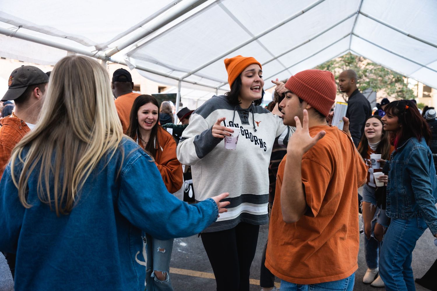 Crowd socializing and mingling under white tent at casual outdoor gathering.