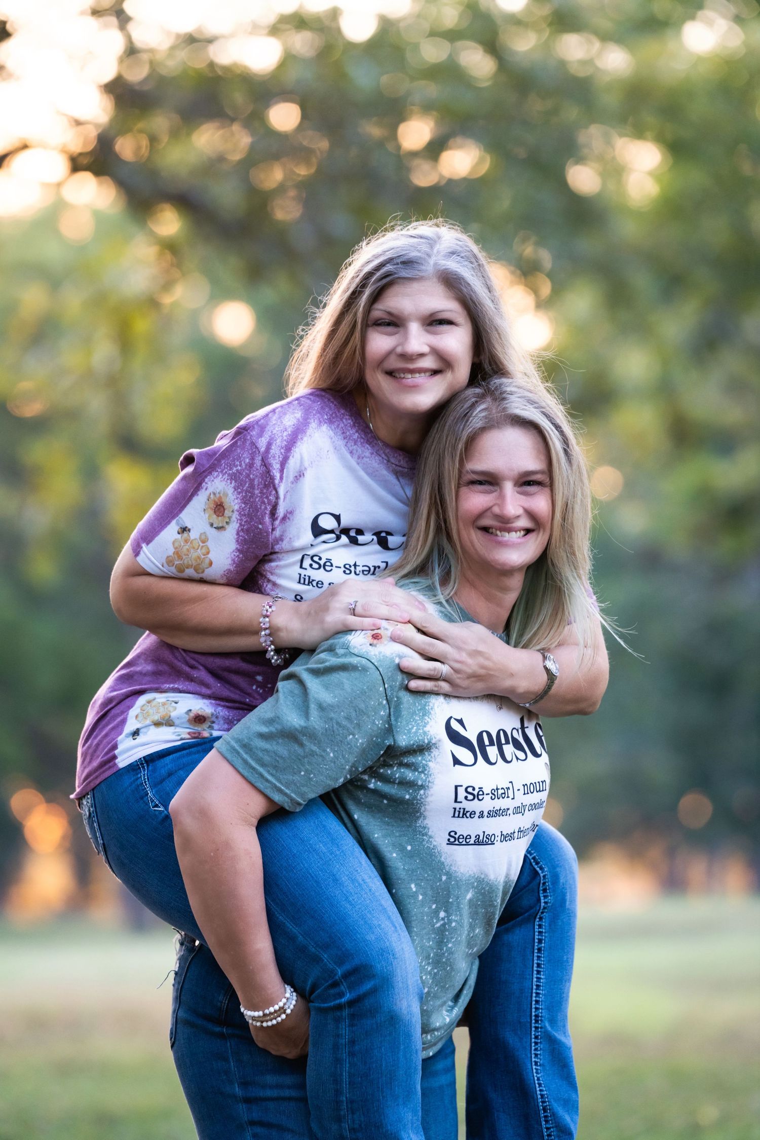 Two people in matching t-shirts share a playful piggyback pose in an outdoor setting.