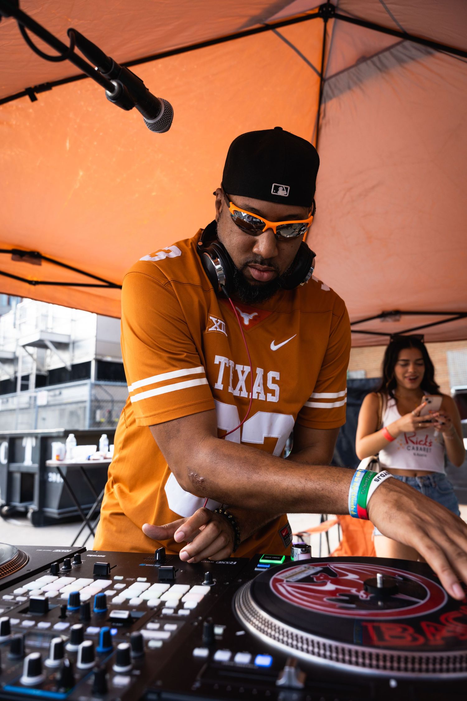 DJ wearing Texas jersey performs at outdoor event under orange tent.