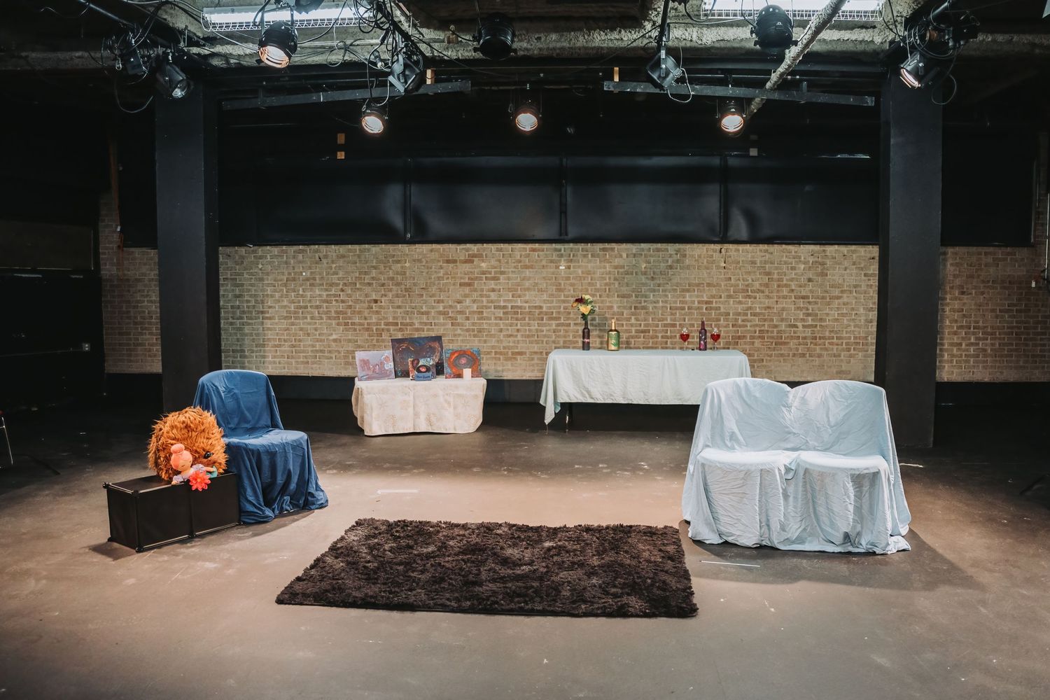 Empty performance space with white-draped tables and a brown rug on the floor.