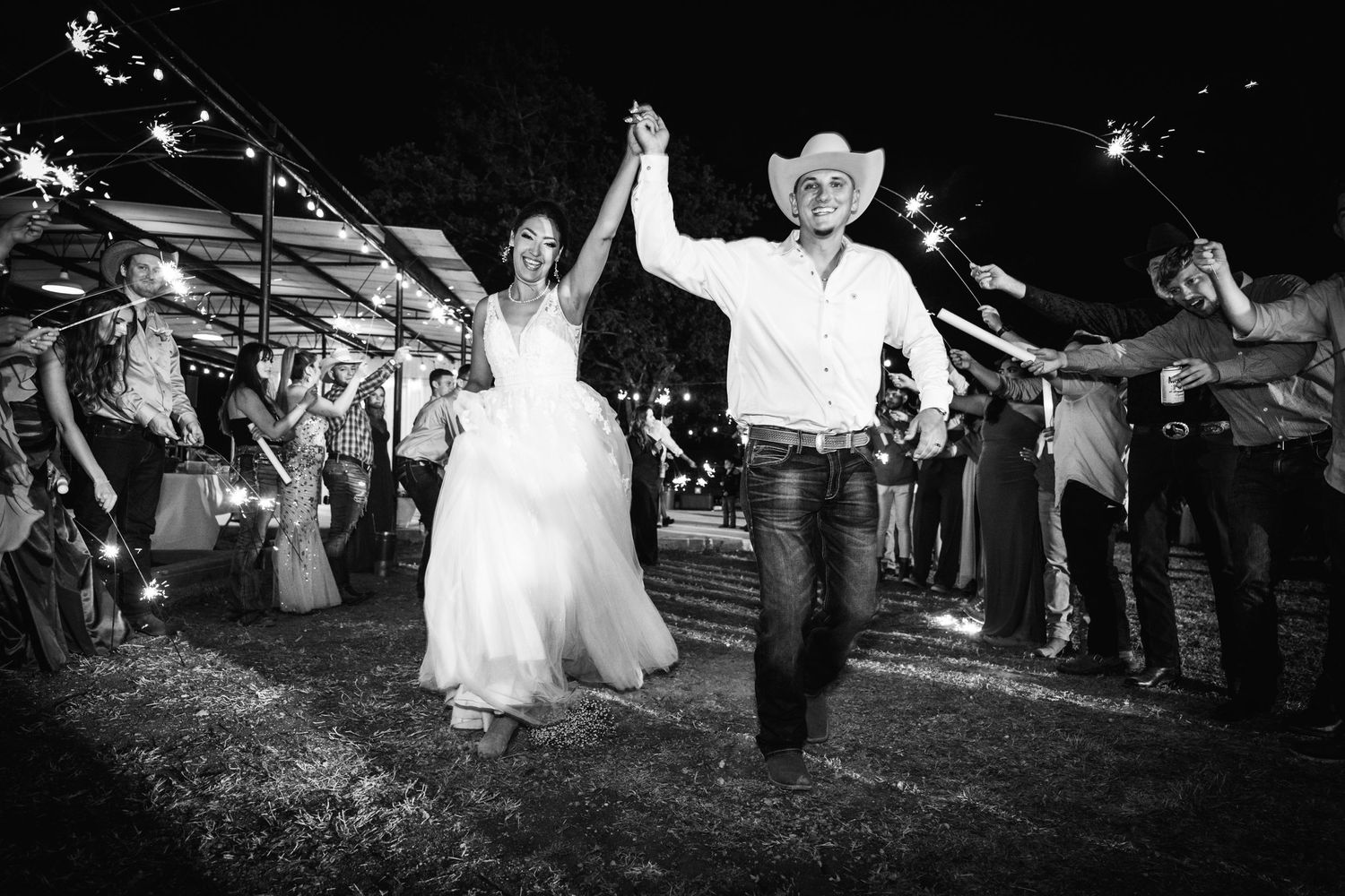Couple exits through sparkler tunnel during nighttime celebration.