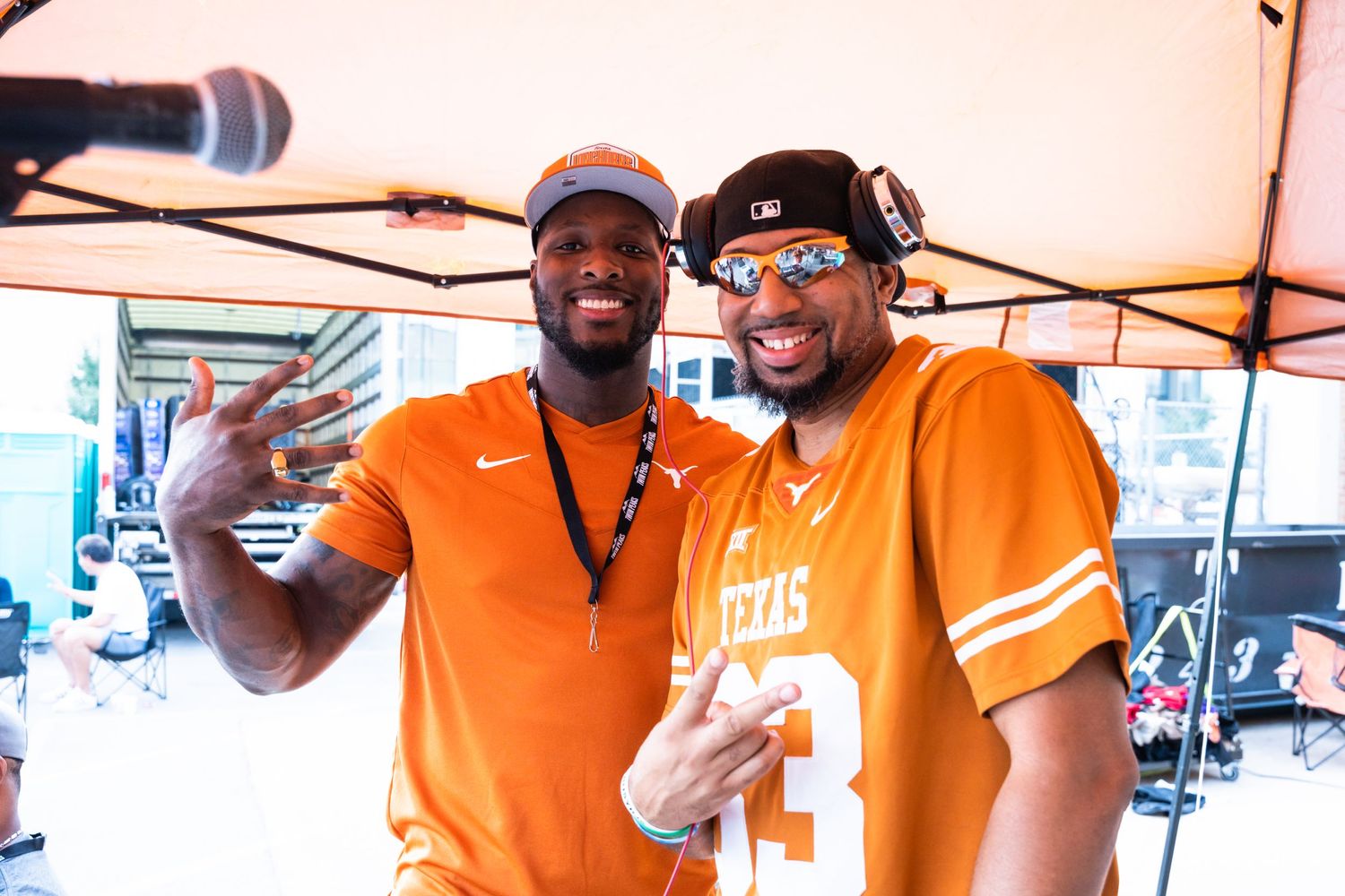 Two people in orange Texas jerseys posing together under event tent with microphones.