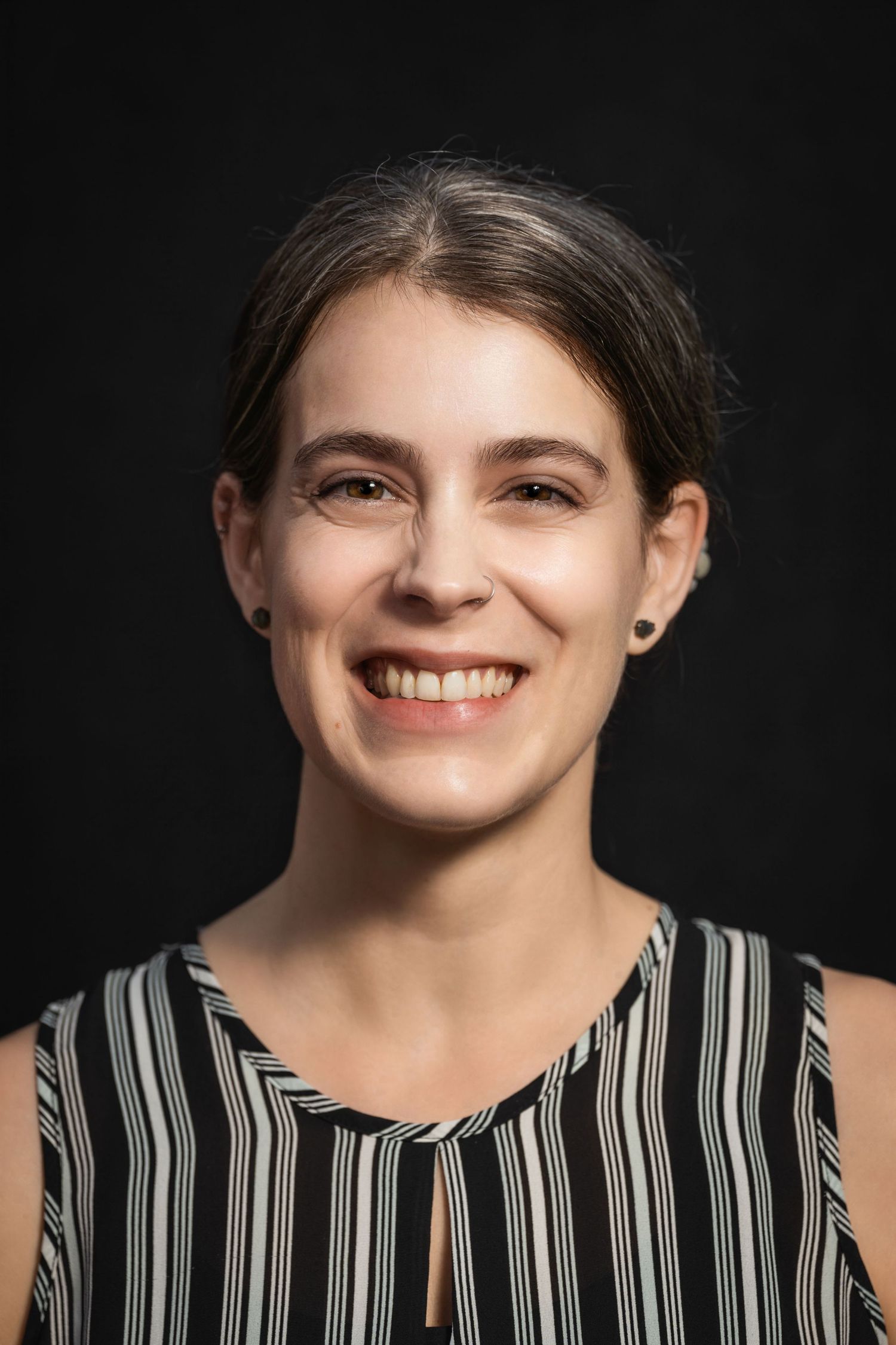 Professional headshot showing person in striped sleeveless top against black background.
