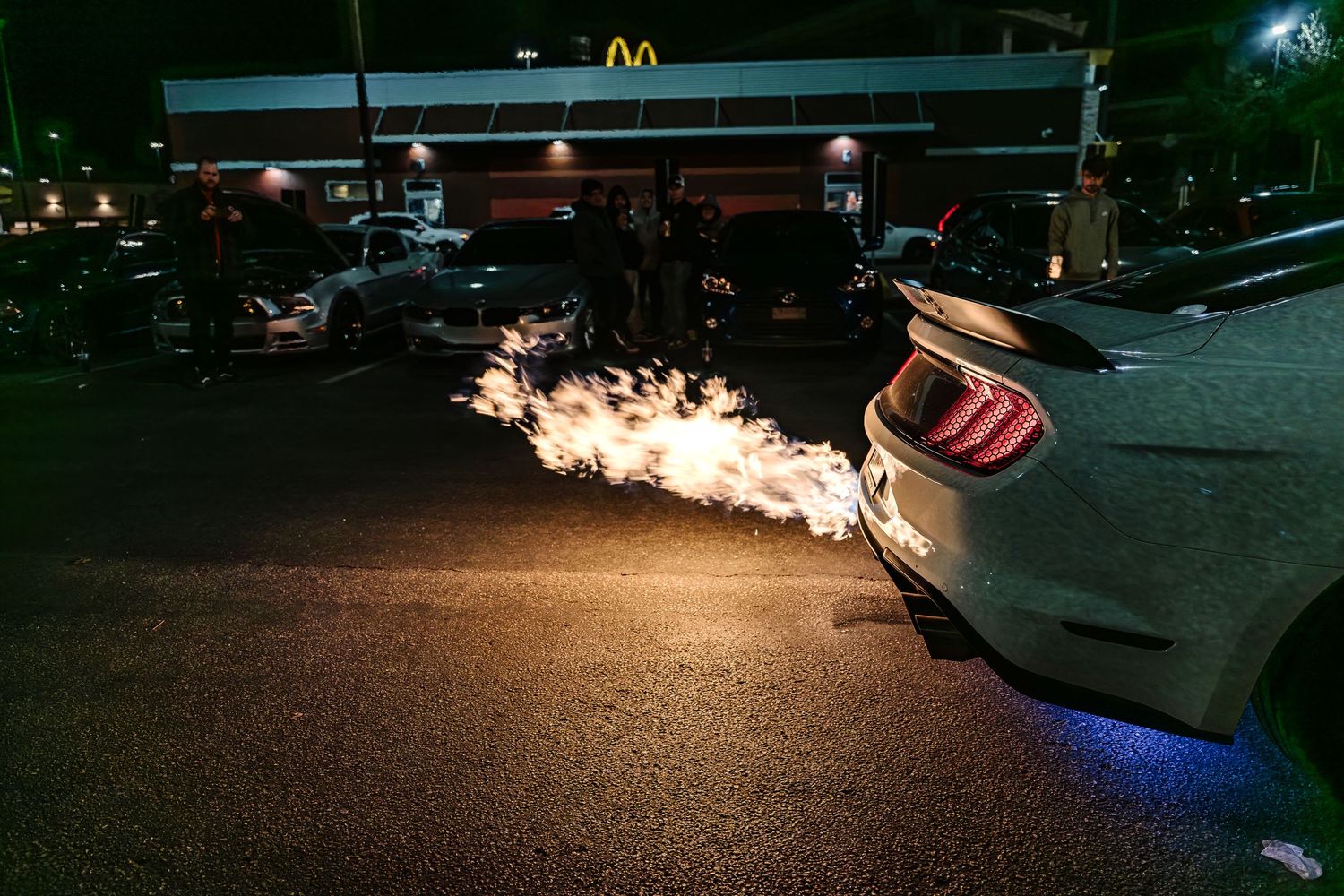 Car exhaust produces dramatic flame effect in dark parking lot at night.