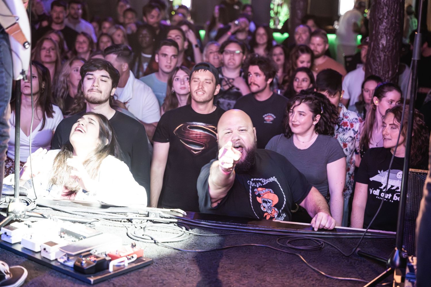 Excited crowd at a music venue watching live performance with stage lighting effects.
