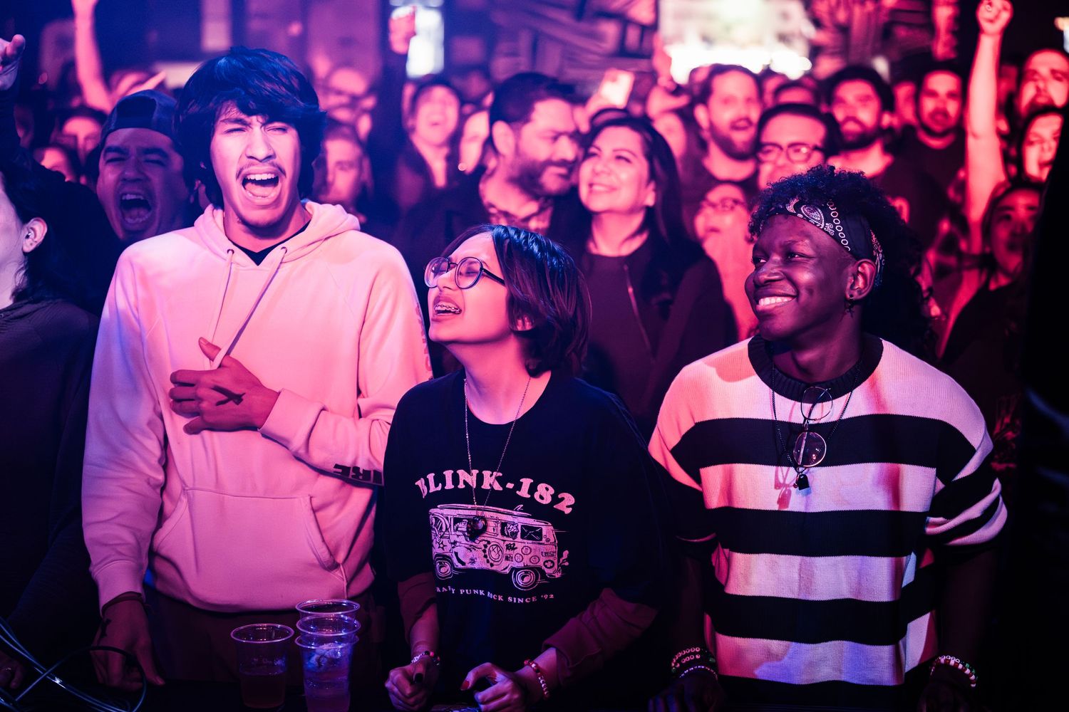 Concert crowd reacting enthusiastically to performance under purple lighting.