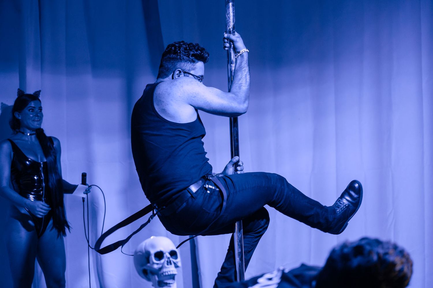 Performer in black costume uses pole prop on dimly lit stage with skeleton decoration.