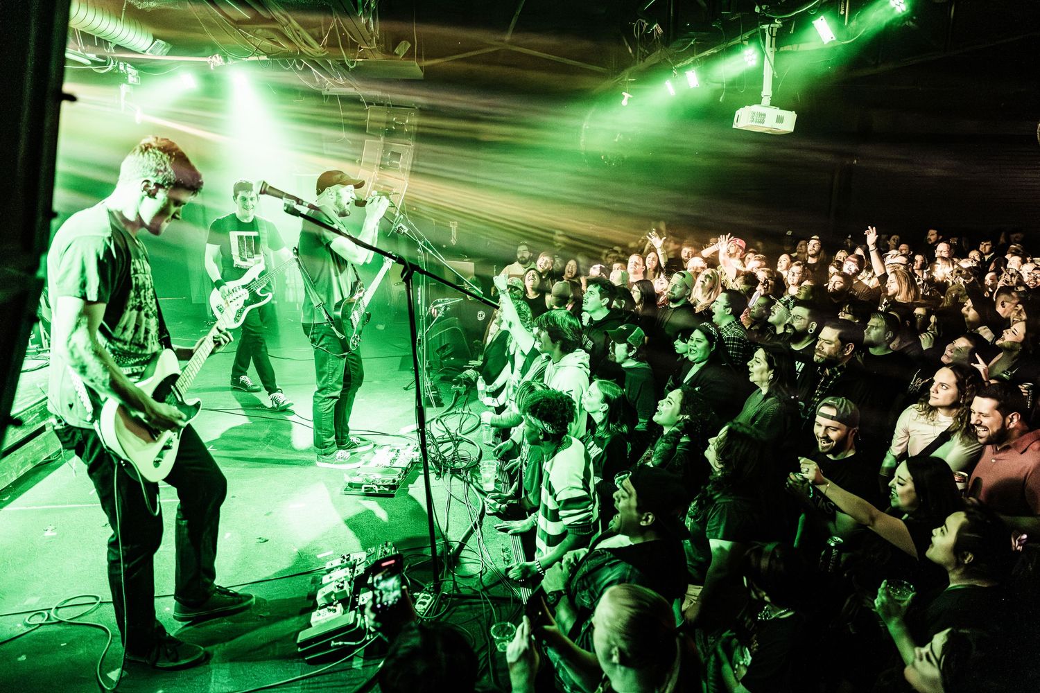 Band performs under green spotlights while crowd cheers at high-energy concert.